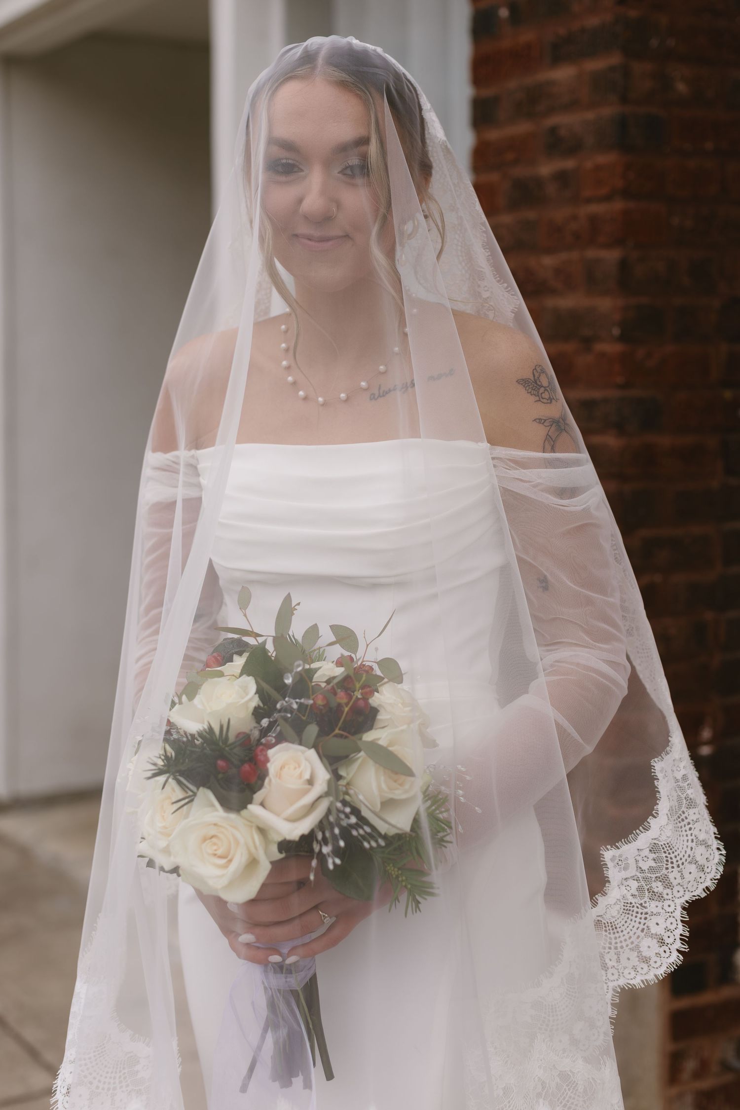 Bride holding white rose bouquet with lace-trimmed veil.