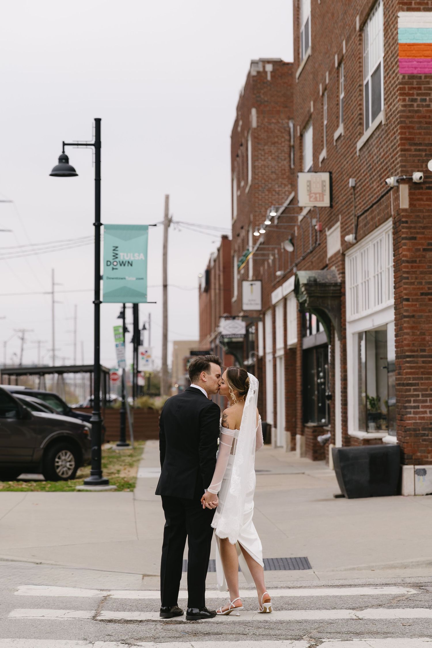 A romantic couple shares a kiss on a quiet brick-lined street corner in a small town business district.