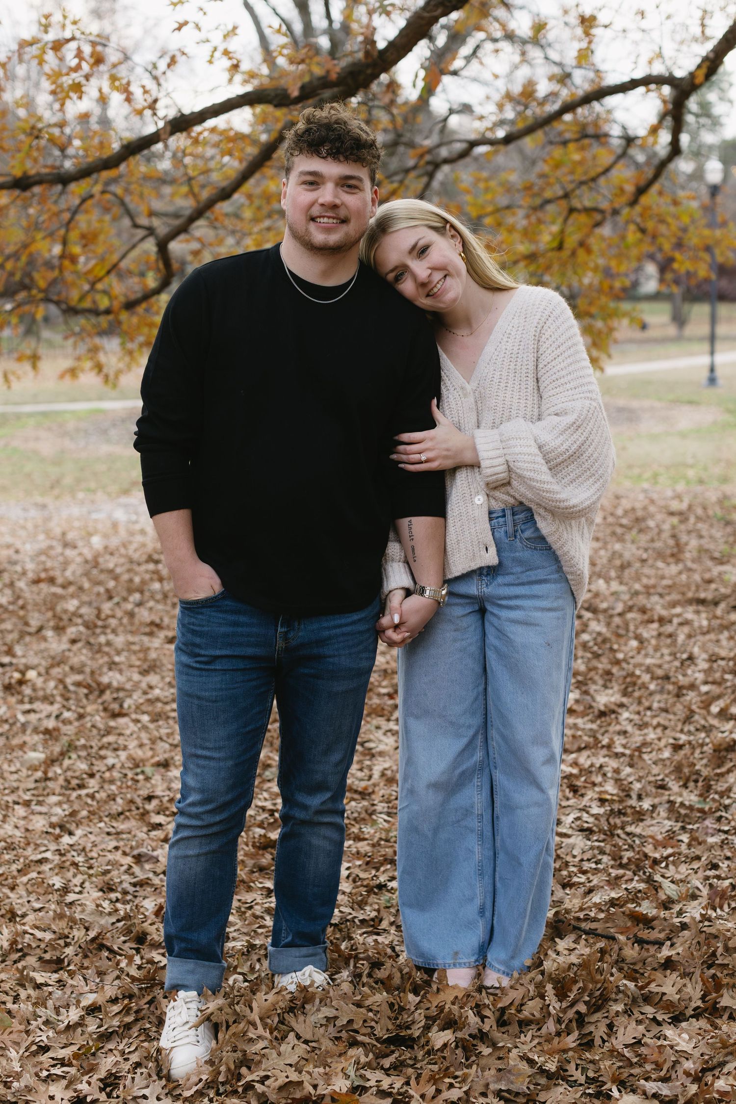 Couple embracing outdoors among fallen autumn leaves wearing coordinated casual outfits.