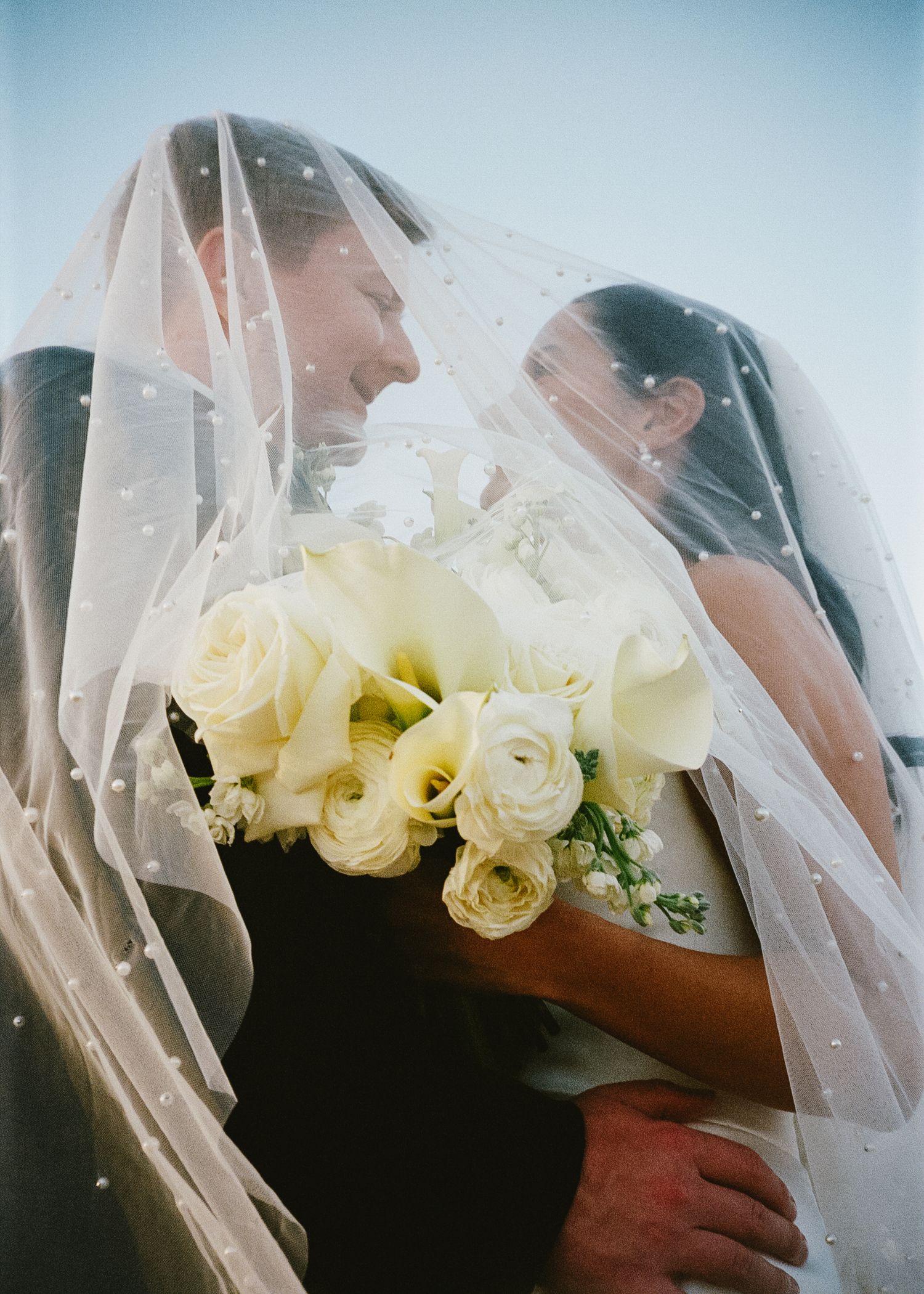 Bridal bouquet of white roses seen through delicate veil in natural light.