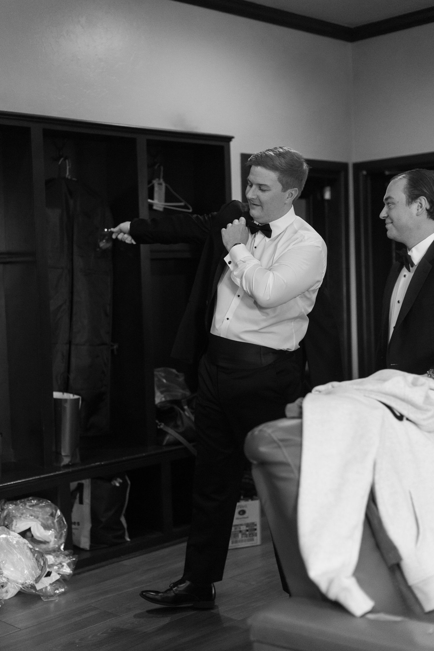 Two men in formal attire getting ready in a dressing room.