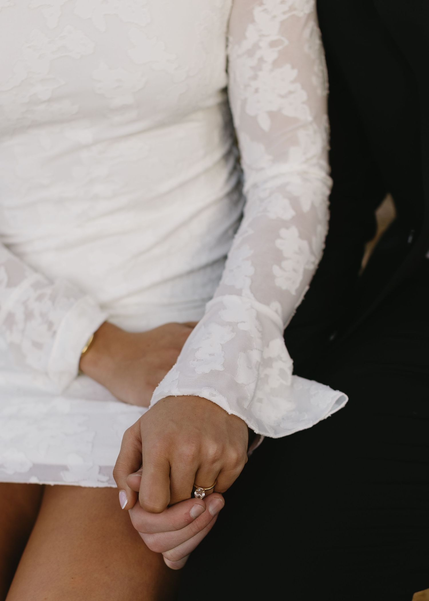 Close-up of hands showing an engagement ring with white lace sleeve details.