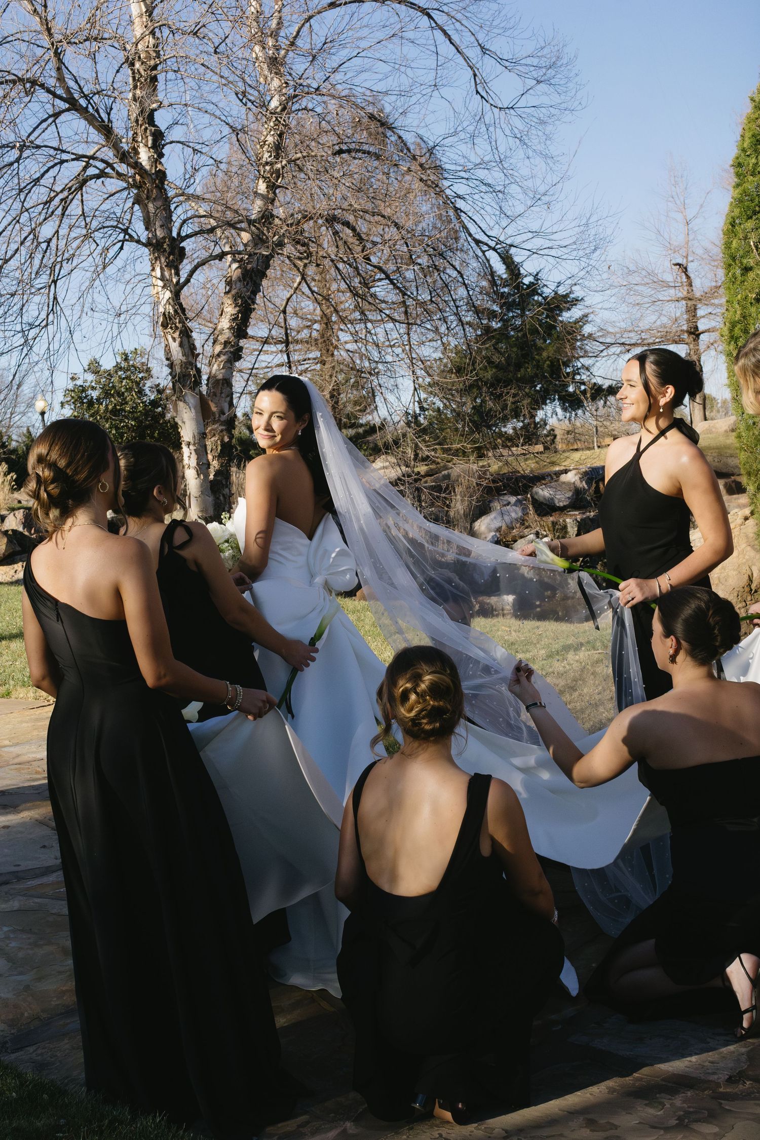 Group in black dresses and formal attire arranging something together outdoors.