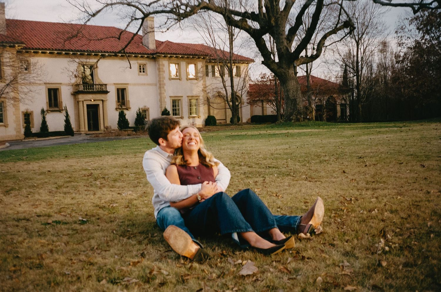 Couple relaxing together on autumn grass with historic buildings in background.