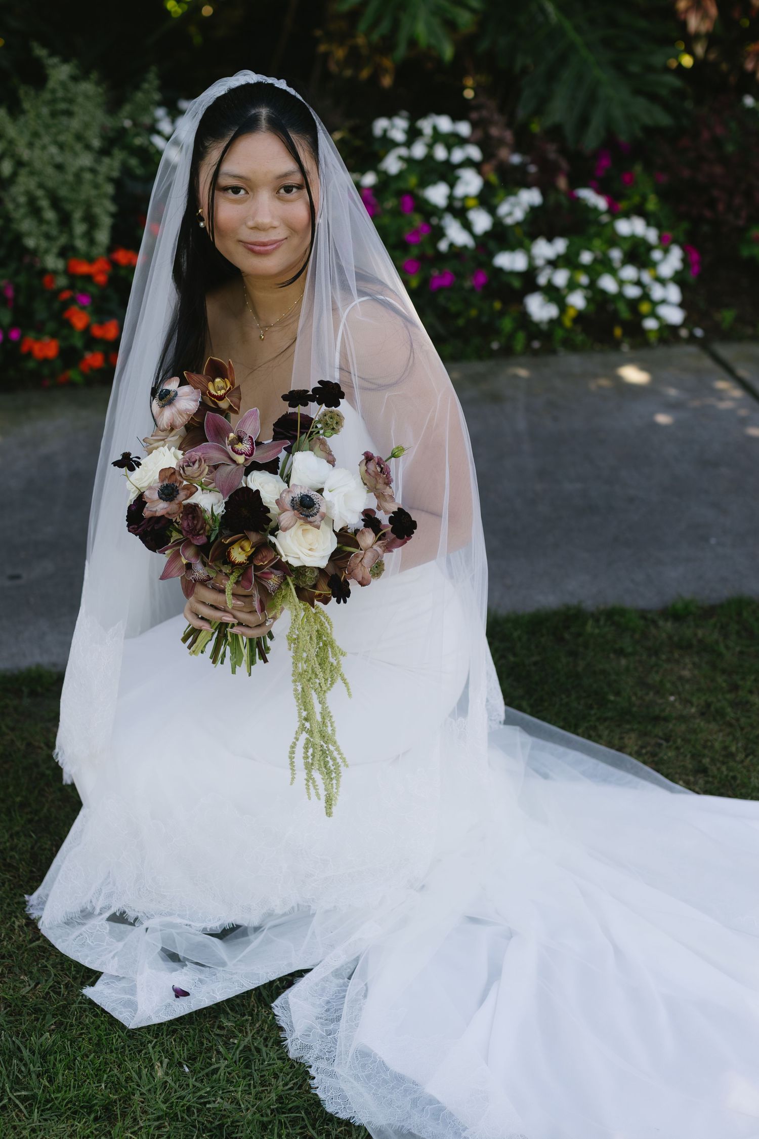 Elegant bride in white dress and veil holds a bouquet with burgundy flowers.