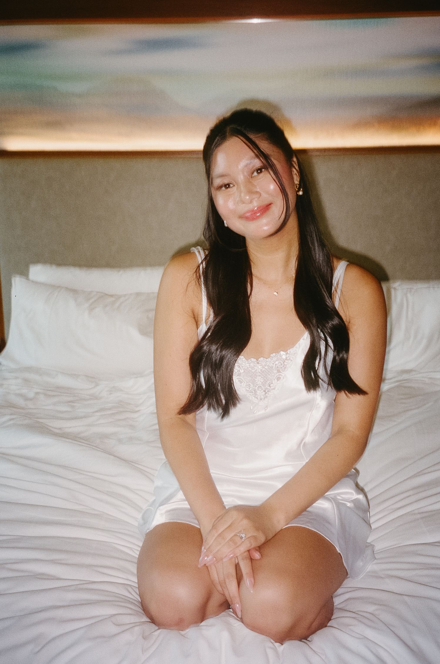 A person in white sits on a bed with crisp white linens.