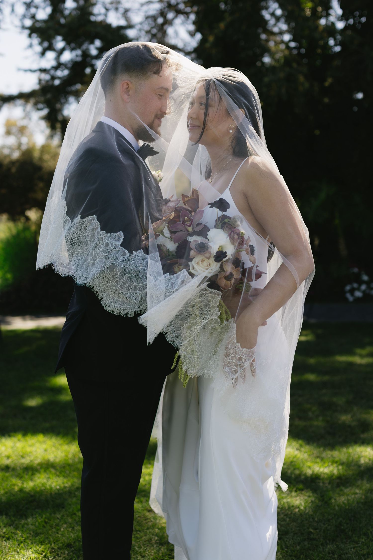 Newlyweds sharing an intimate moment in sunlit garden with bridal bouquet.