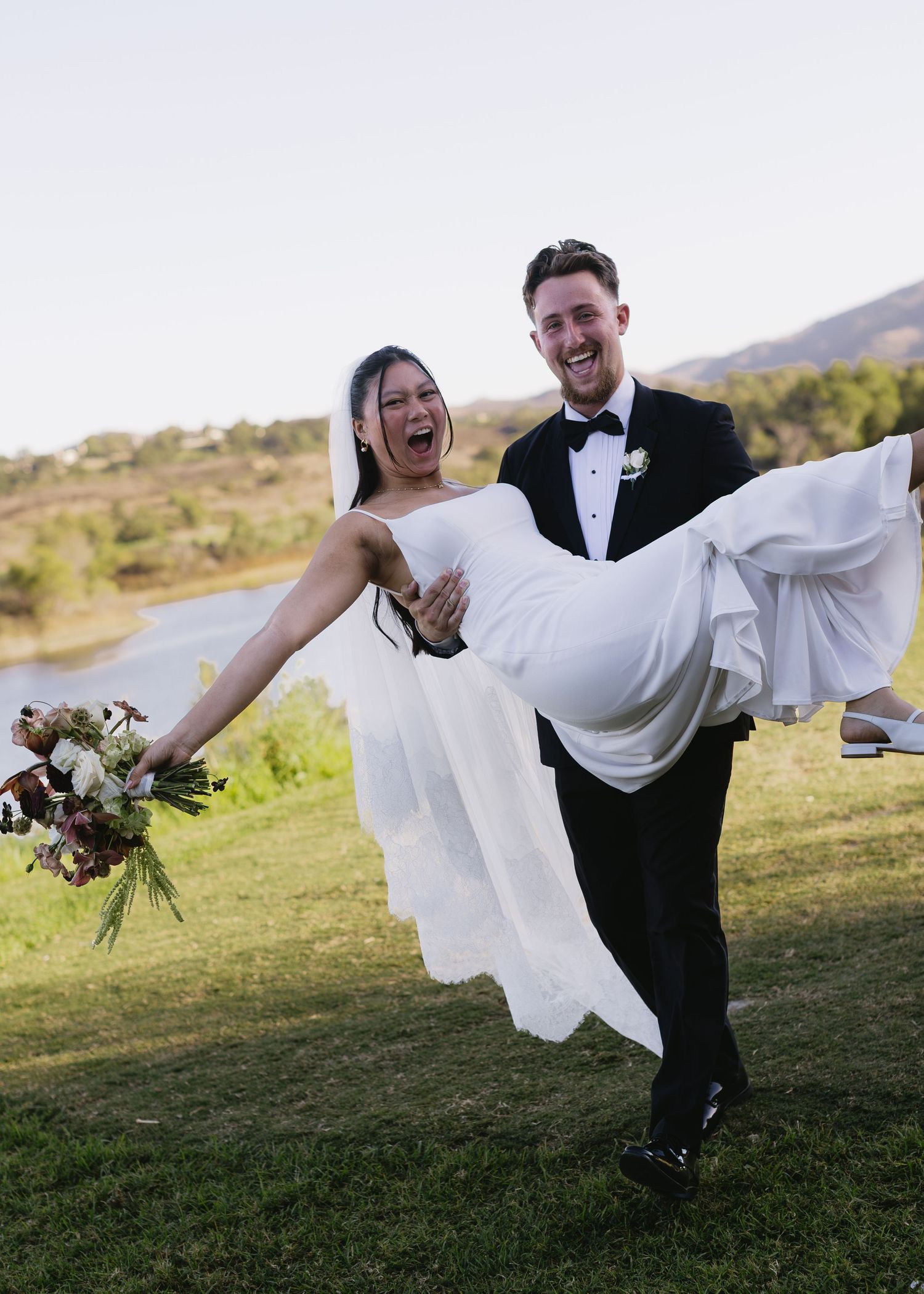 A joyful wedding moment captured as the groom carries the bride while she holds her bouquet.