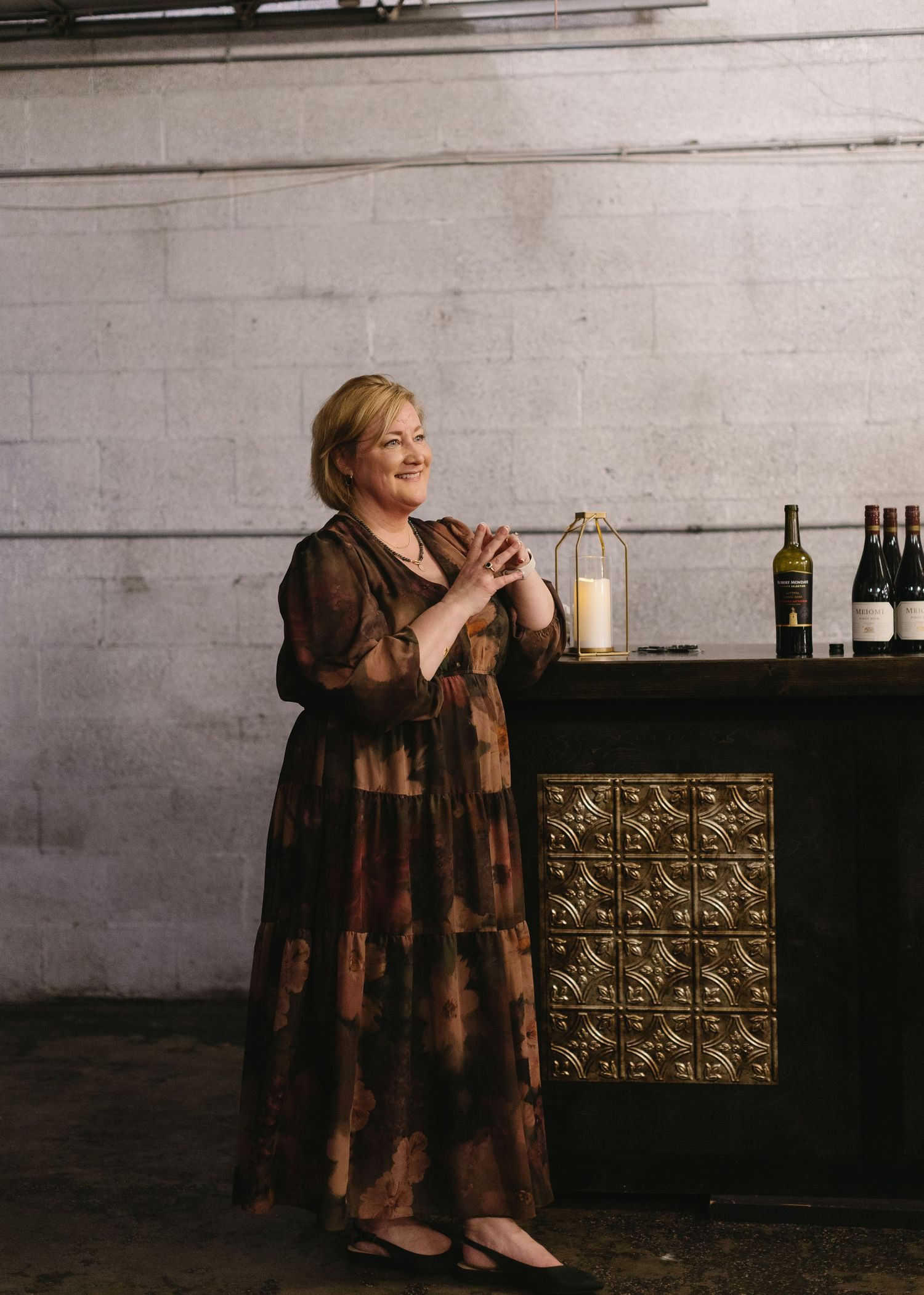 Woman in brown patterned dress standing next to decorative bar cabinet.