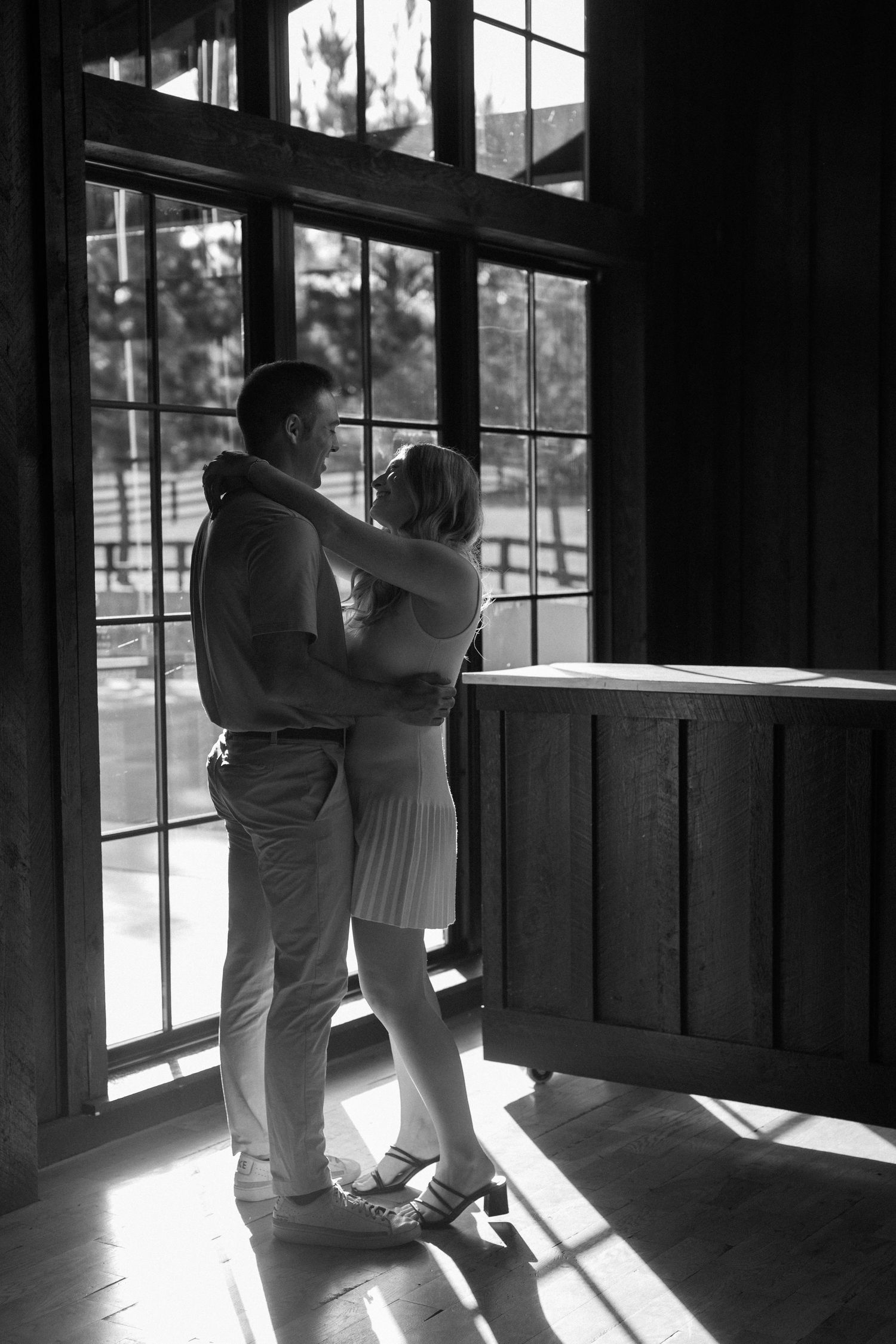 Silhouetted couple dancing in sunlit room with large windows.