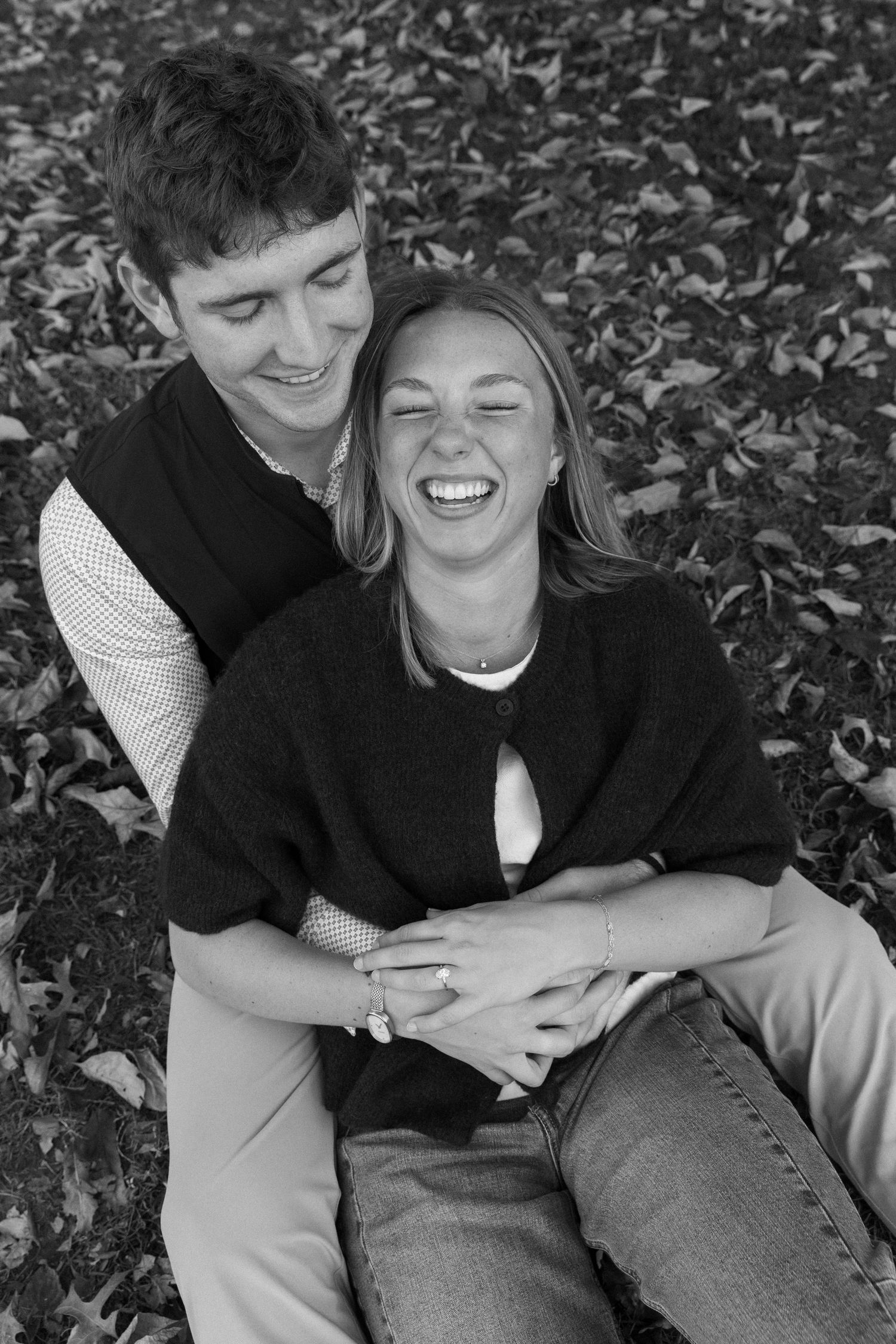 Two people laughing together while sitting on autumn leaves.