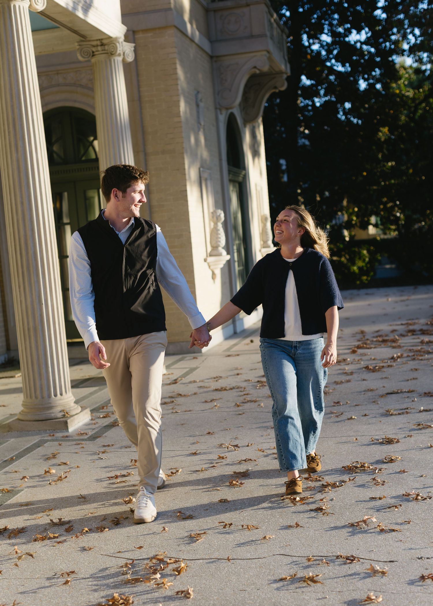 Sequence of a person walking on a paved surface with fallen autumn leaves and white columns in the background.