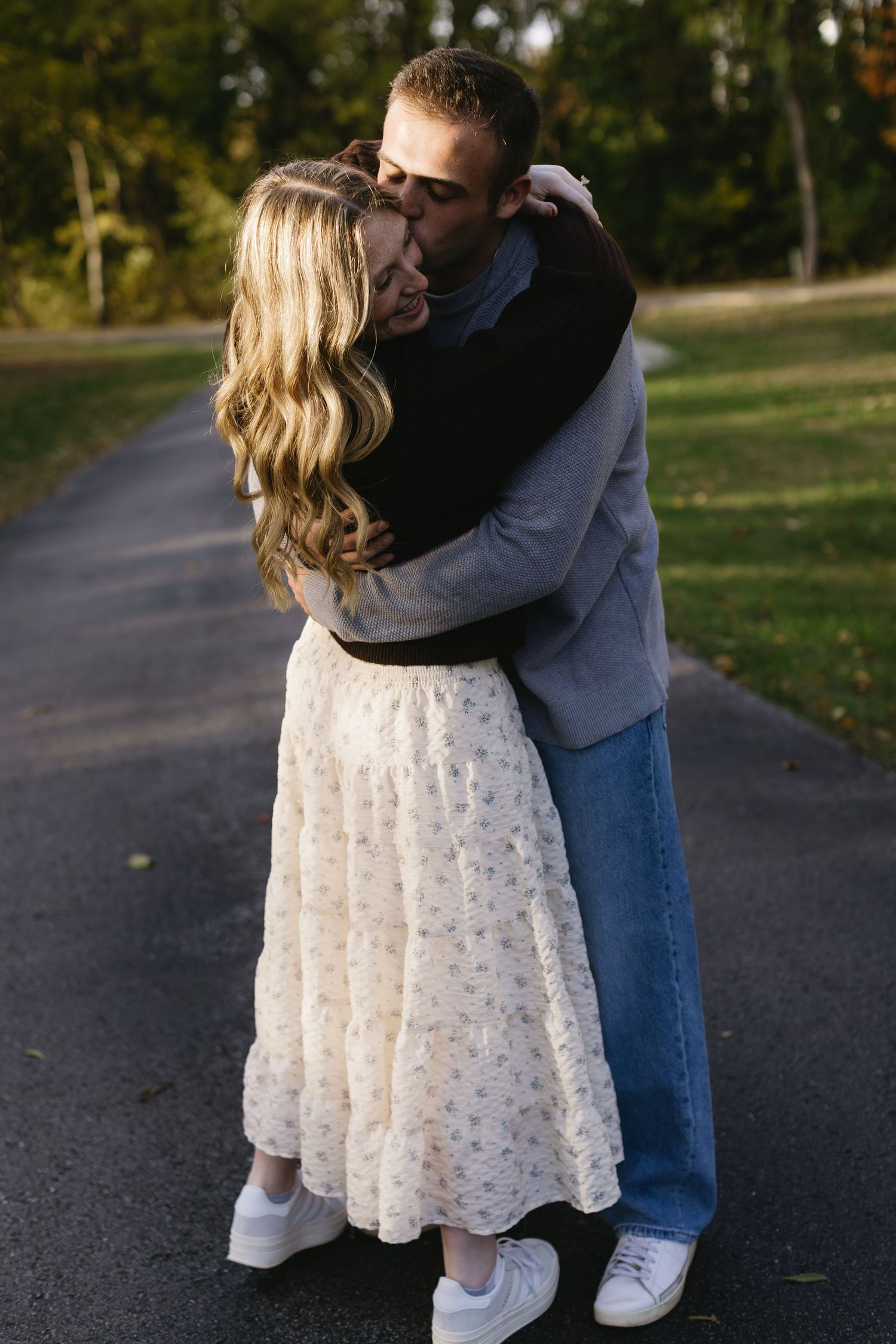 A couple embracing on a path in an autumn park setting wearing casual clothing and white shoes.
