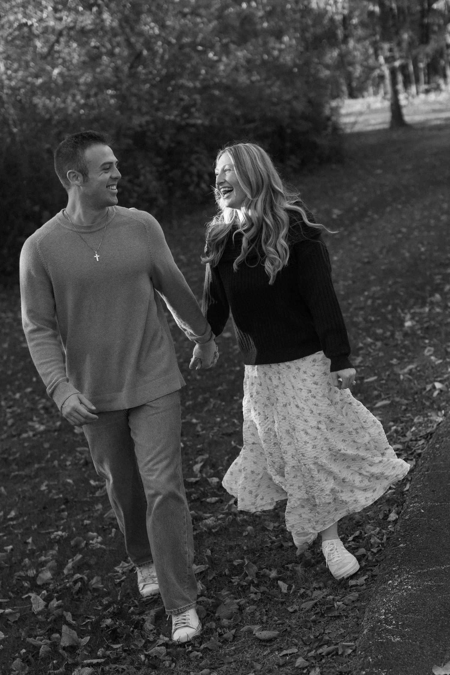 Black and white photo of a couple walking through fallen leaves in autumn.