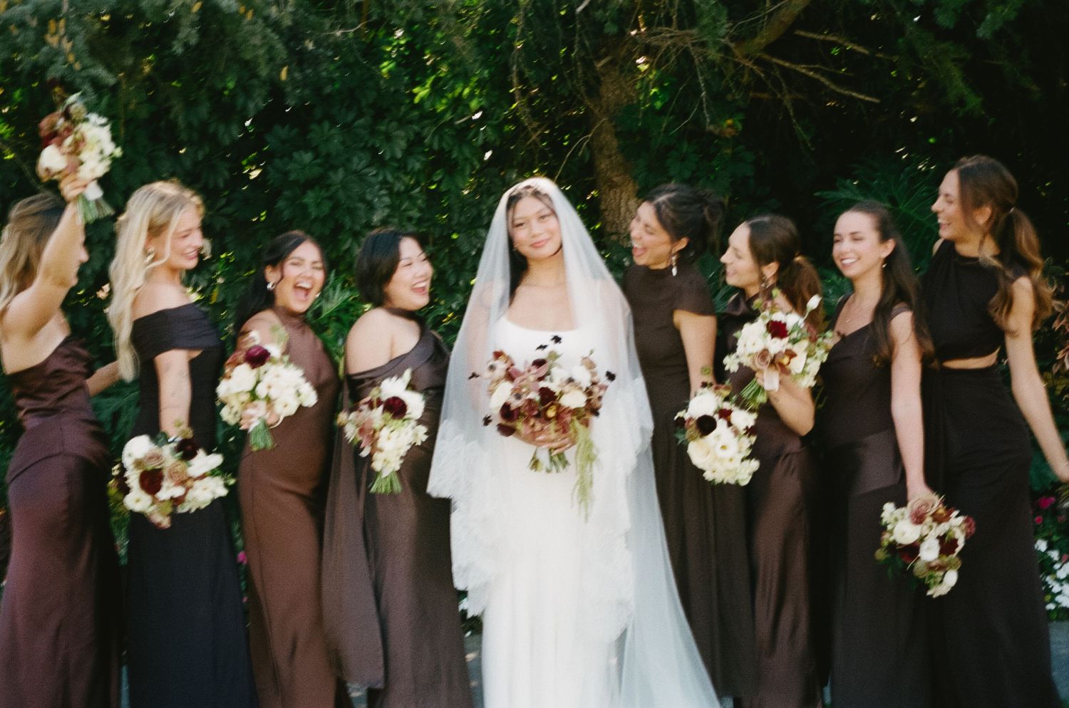 Wedding party lineup outdoors with bridesmaids in brown dresses and floral bouquets.