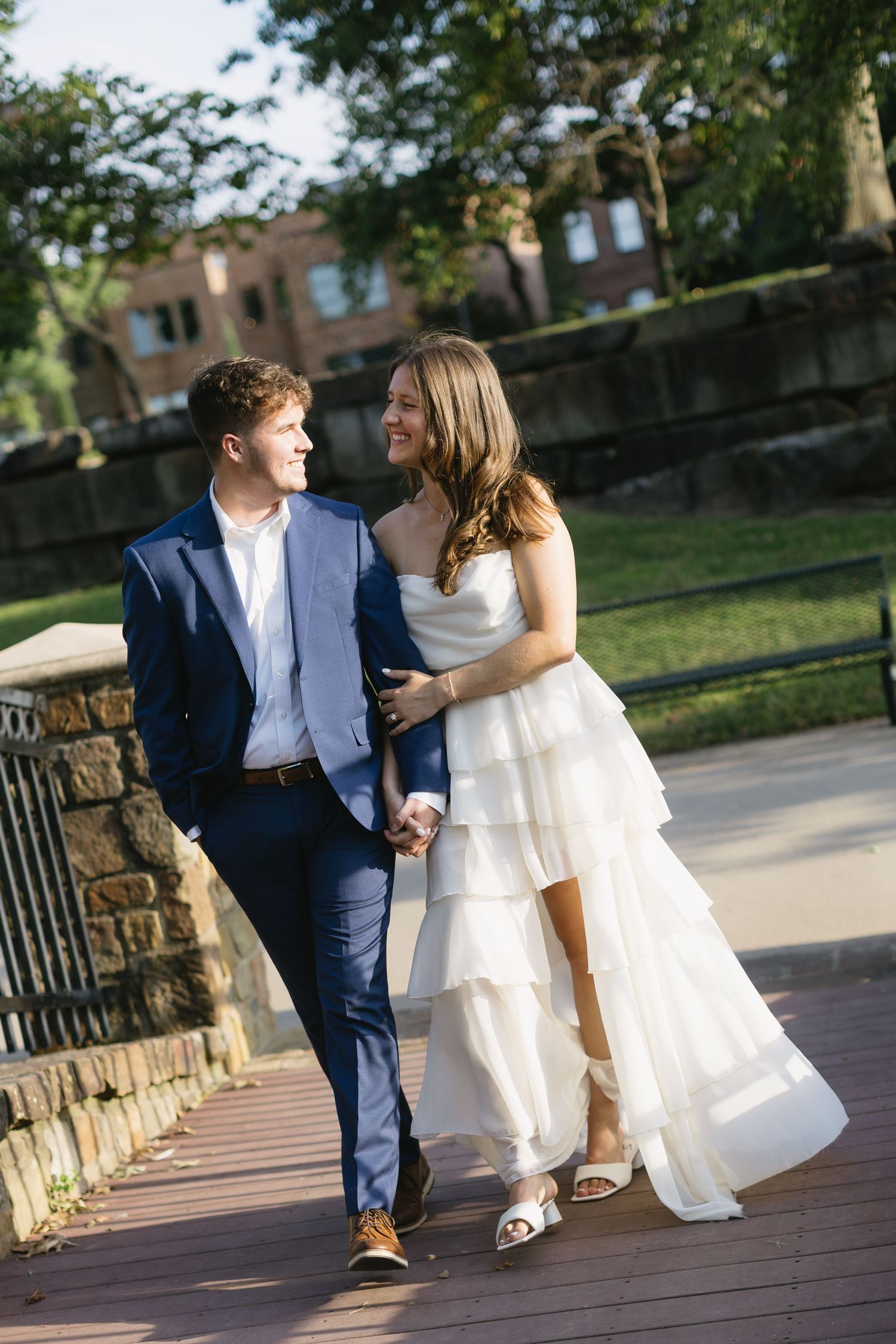 A couple walking and laughing together on a stone pathway in formal attire.