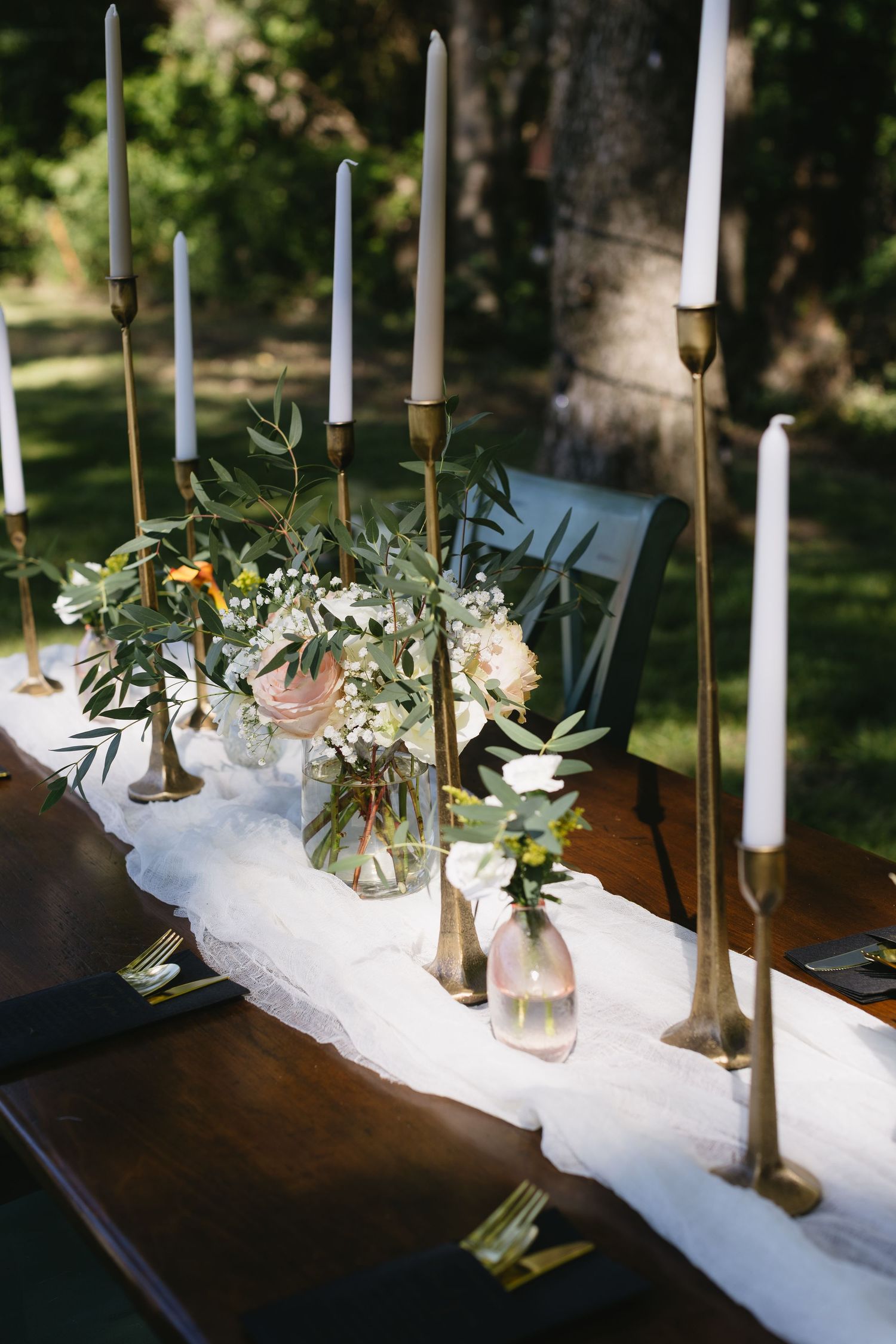 Elegant table setting with white taper candles and small floral arrangements on a wooden surface.