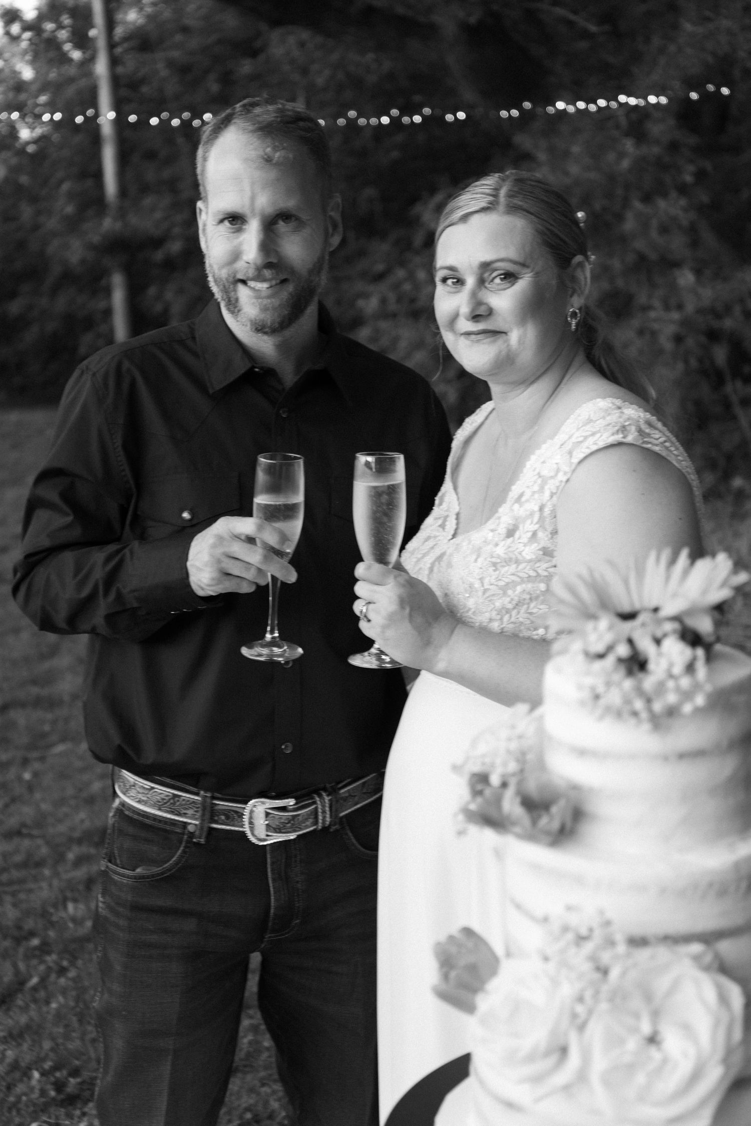 A black and white photo of newlyweds sharing a moment while cutting their wedding cake together.