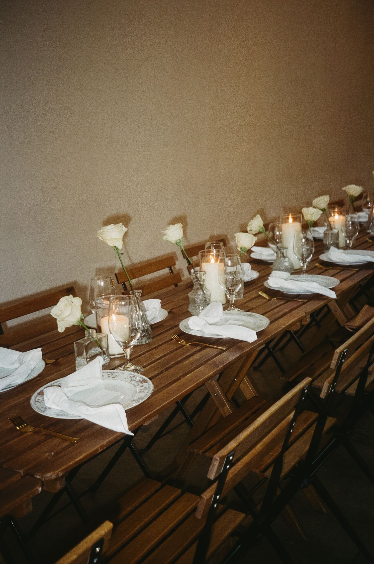 Rustic wooden dining tables set with white plates, candles, and floral centerpieces for an elegant event.