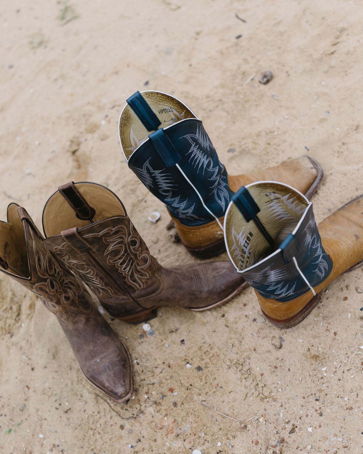 Weathered brown and black cowboy boots arranged artistically on sandy ground.