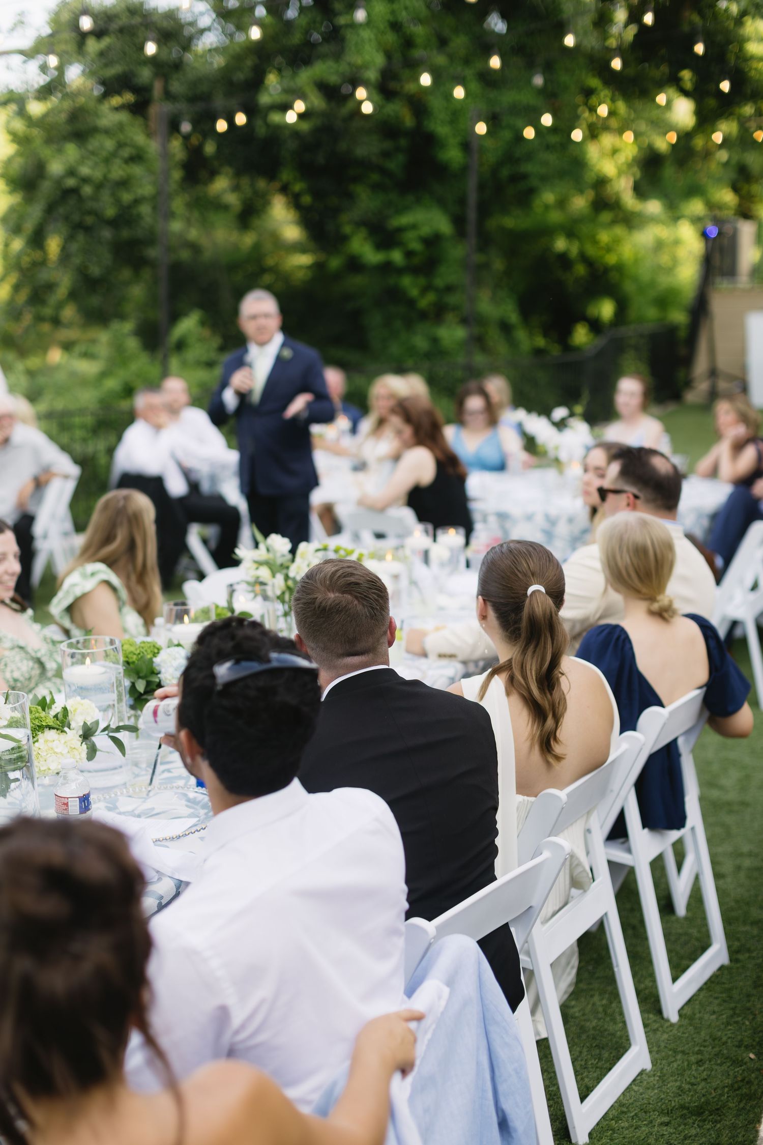 An elegant outdoor wedding reception with white tables and floral centerpieces on a manicured lawn.