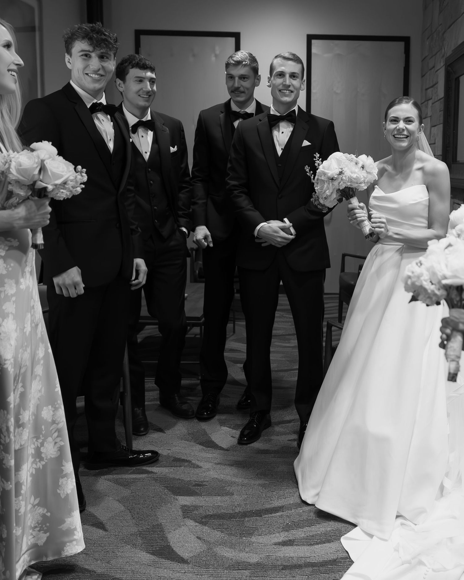 Wedding party in formal attire lined up and smiling in an elegant indoor venue.