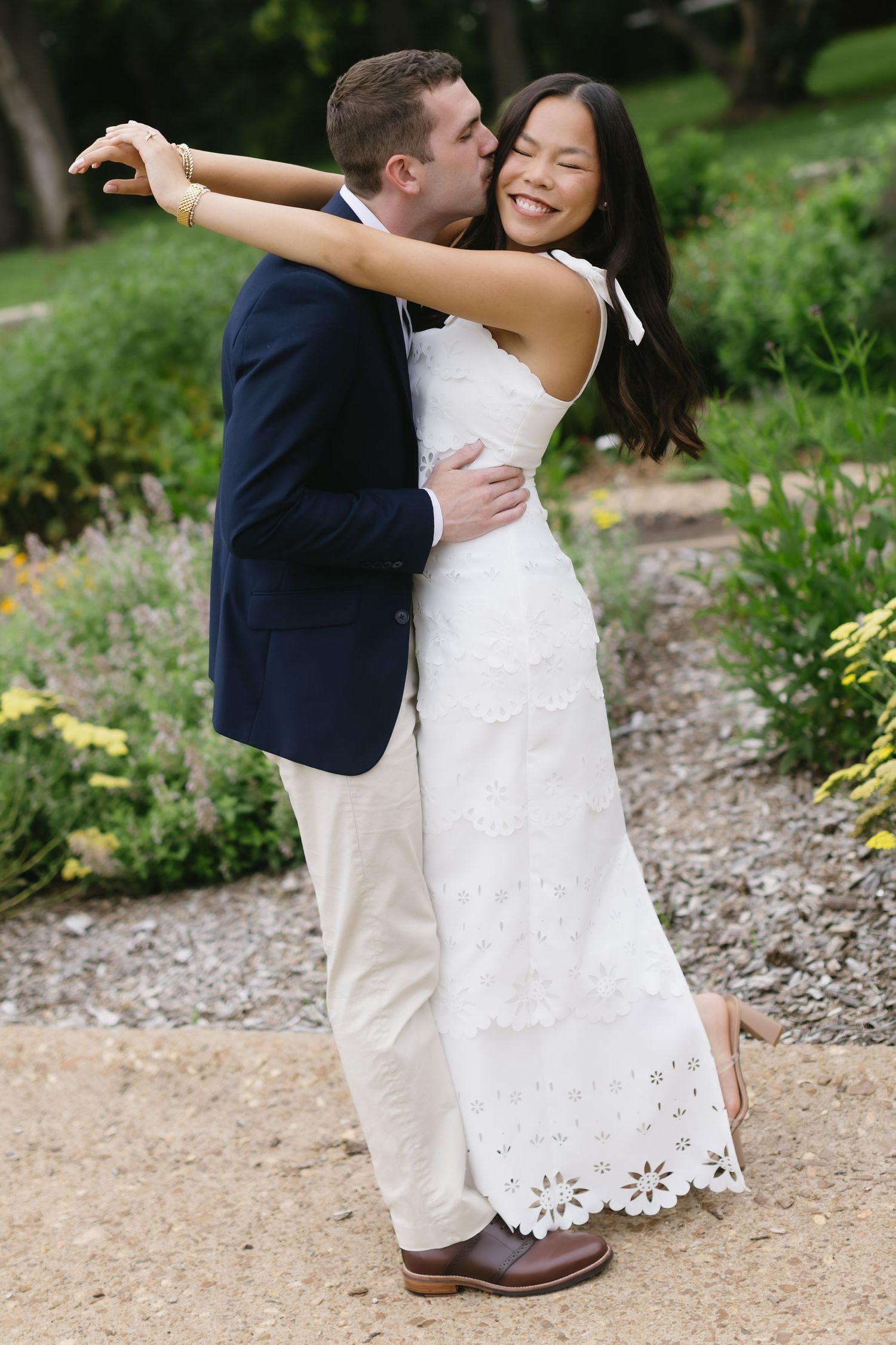 A couple dances playfully on a gravel path surrounded by lush garden greenery.
