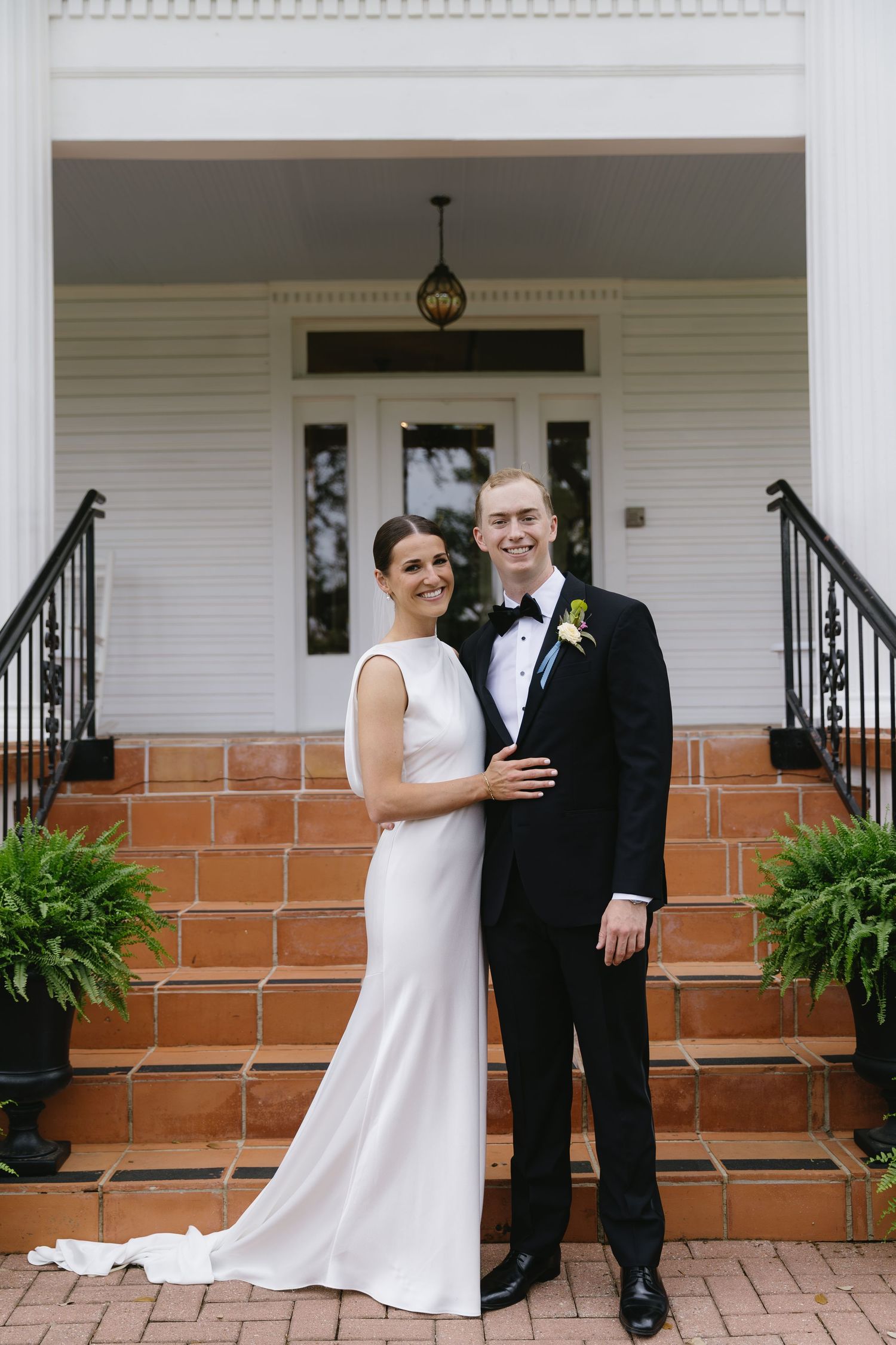 Couple shares an intimate moment on a white porch with brick steps and decorative columns.