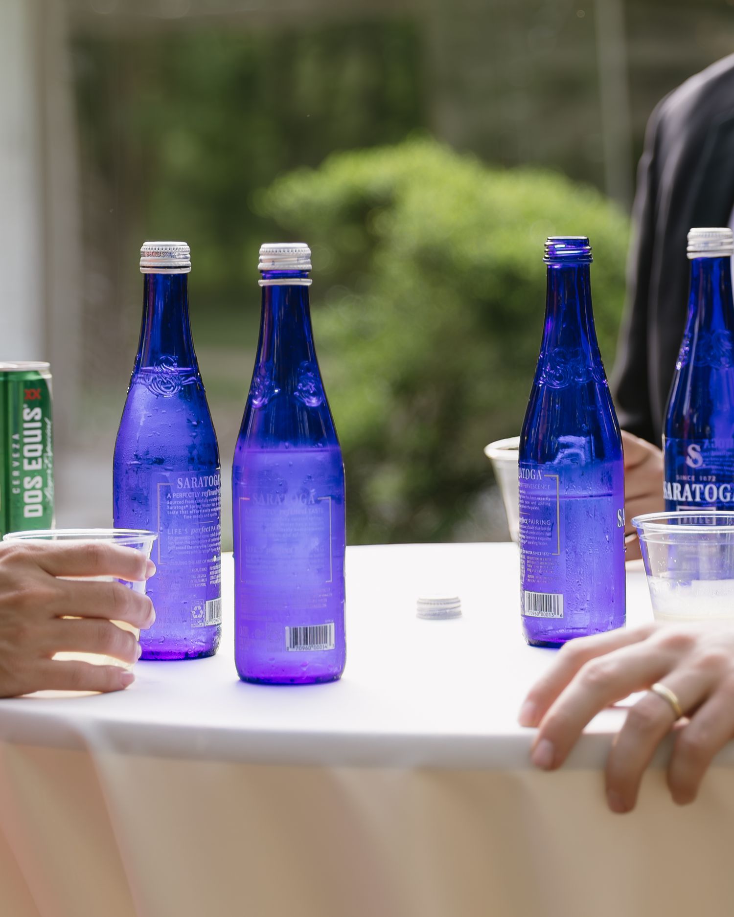 Blue glass water bottles arranged on white table at outdoor event.