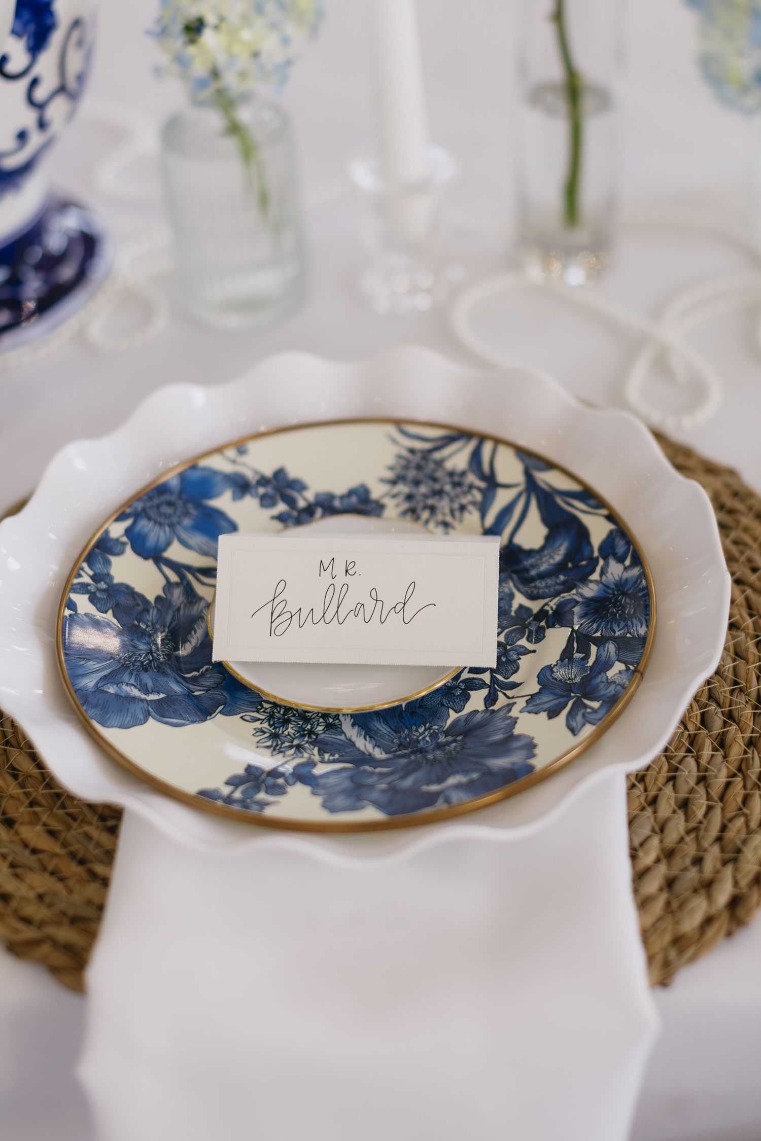 Elegant table setting with blue and white china plates on woven placemats with name cards.