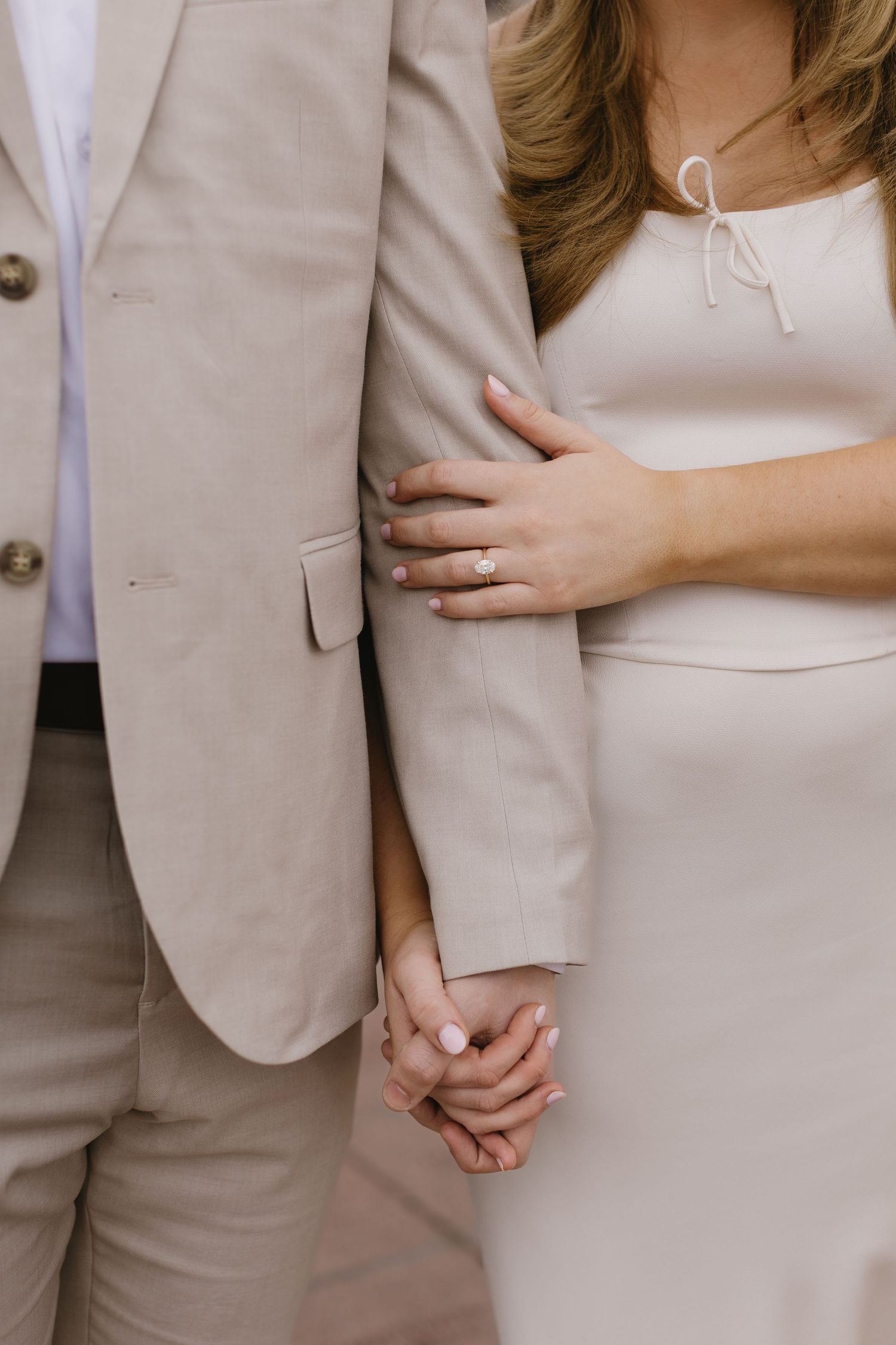 Close-up details of a couple in beige and white formal wear embracing.