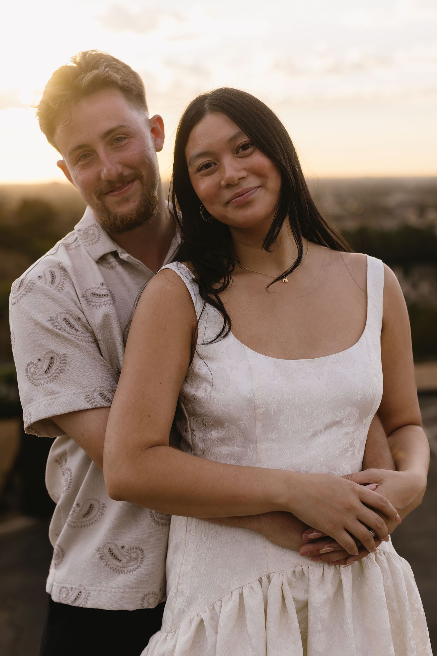A couple shares an intimate moment at sunset against a scenic backdrop.