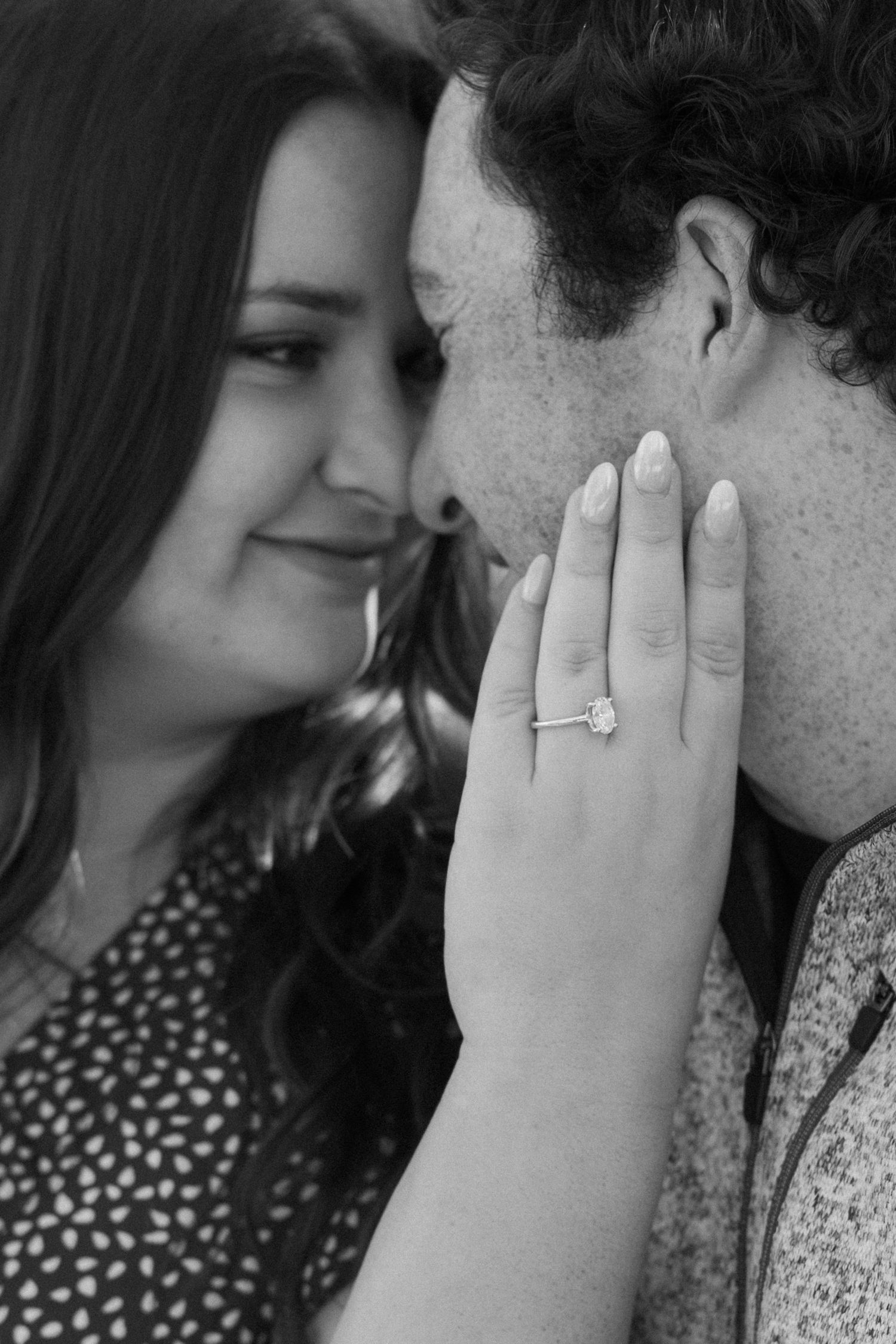 Black and white close-up of a couple showing engagement ring and tender moment.