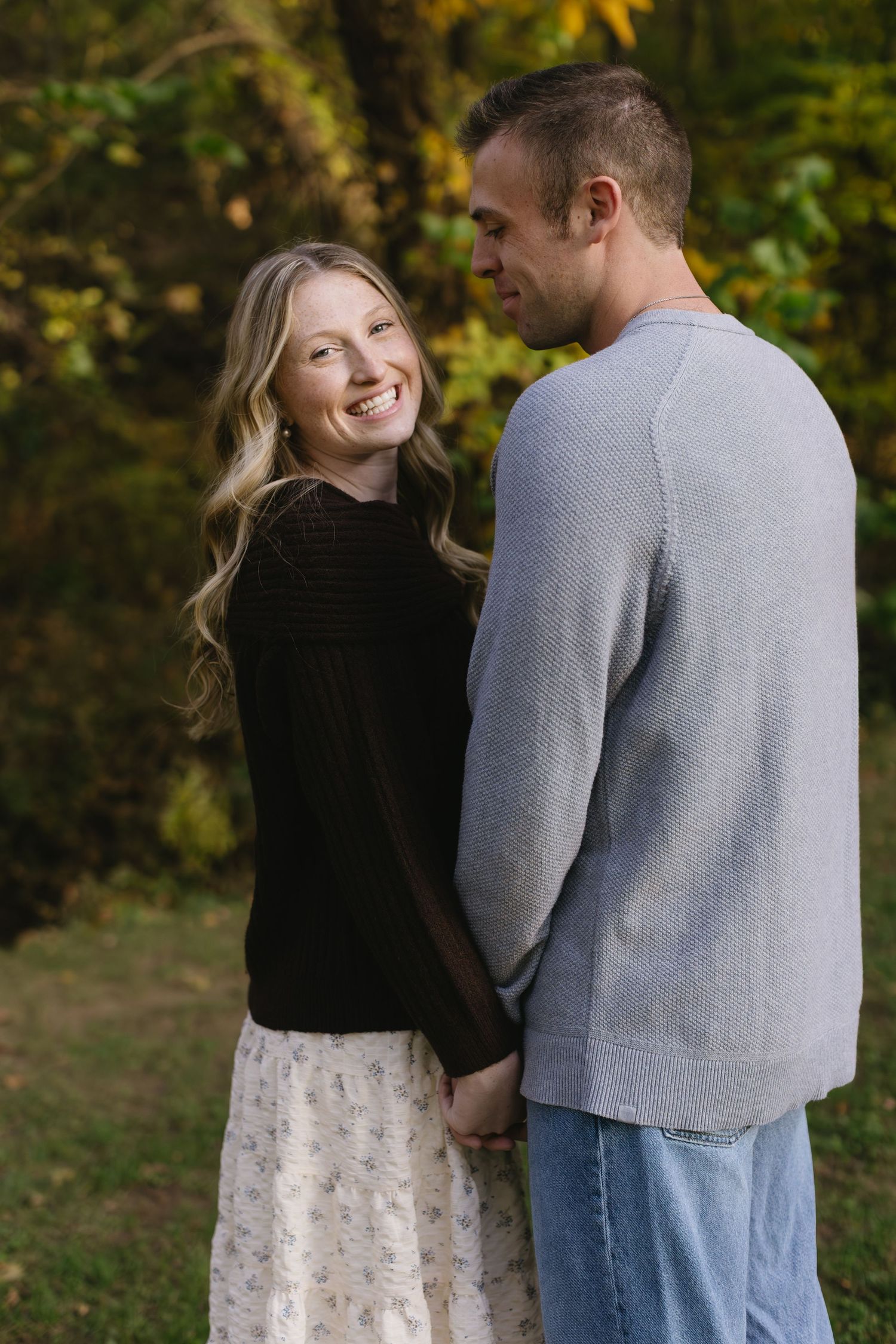 A couple shares a joyful moment together in an autumn setting with fall foliage.