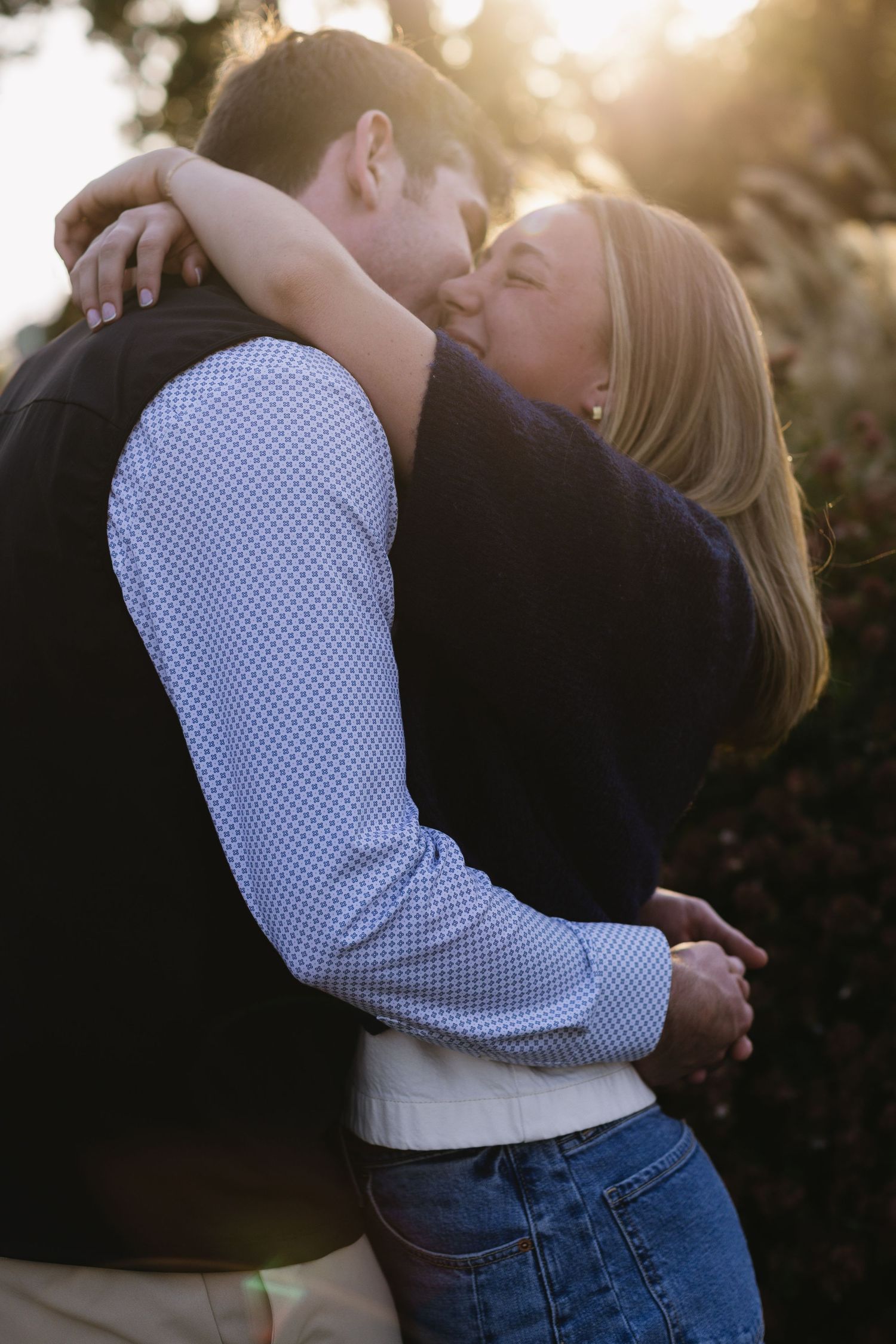 A romantic couple embraces in warm sunset light, with one wearing a checkered shirt and jeans.