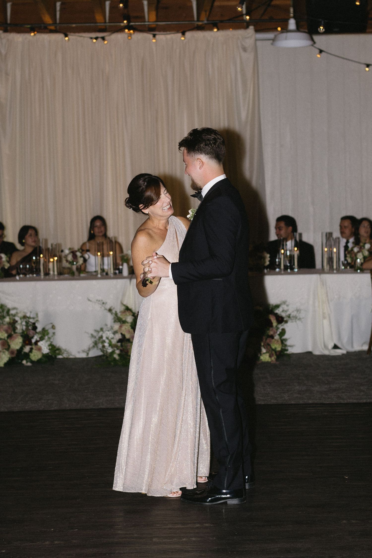 Intimate first dance moment at a wedding reception with elegant backdrop and head table.