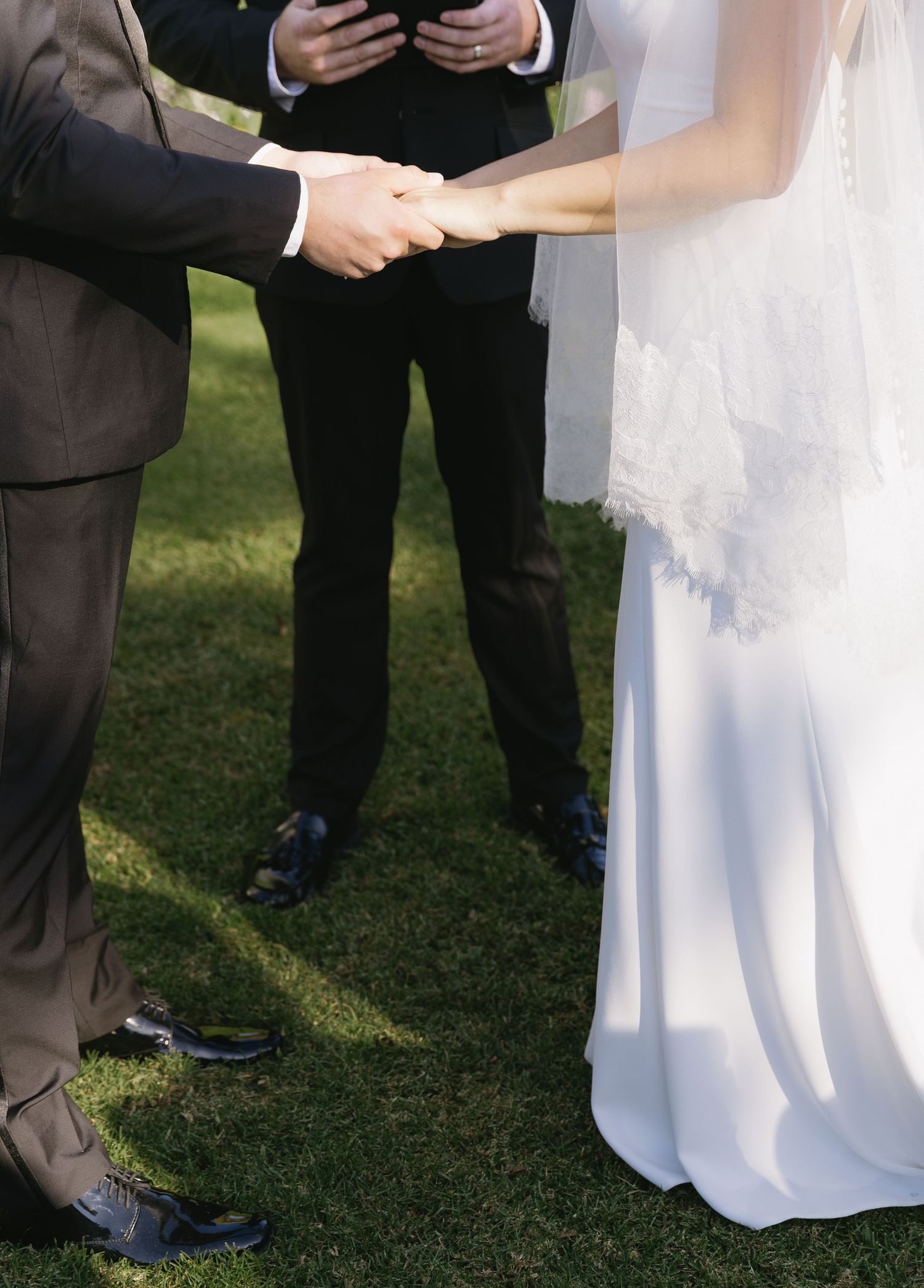 Close-up of hands during a wedding ceremony exchange on green grass.
