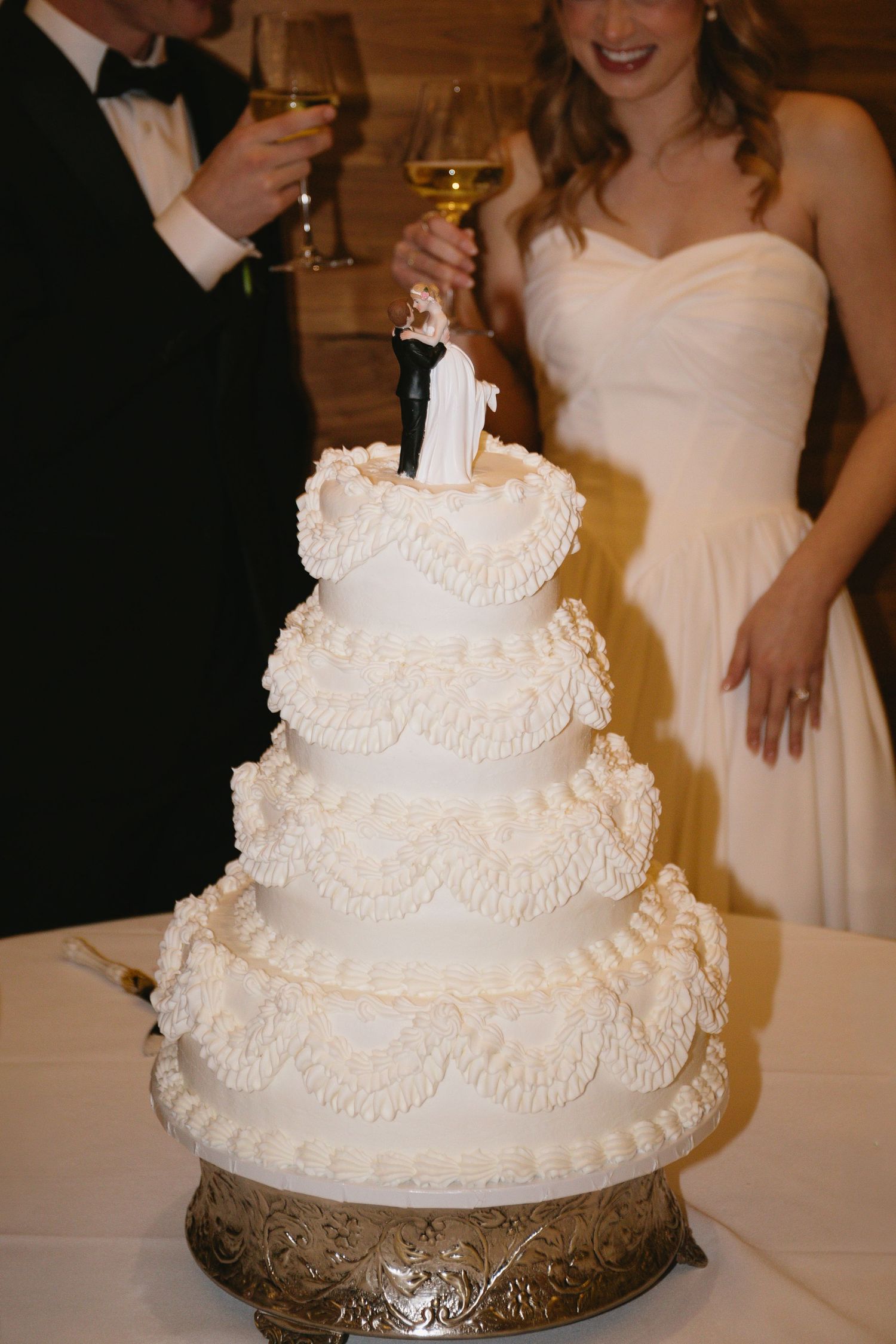 An elegant white tiered wedding cake with delicate piped details on a silver stand.