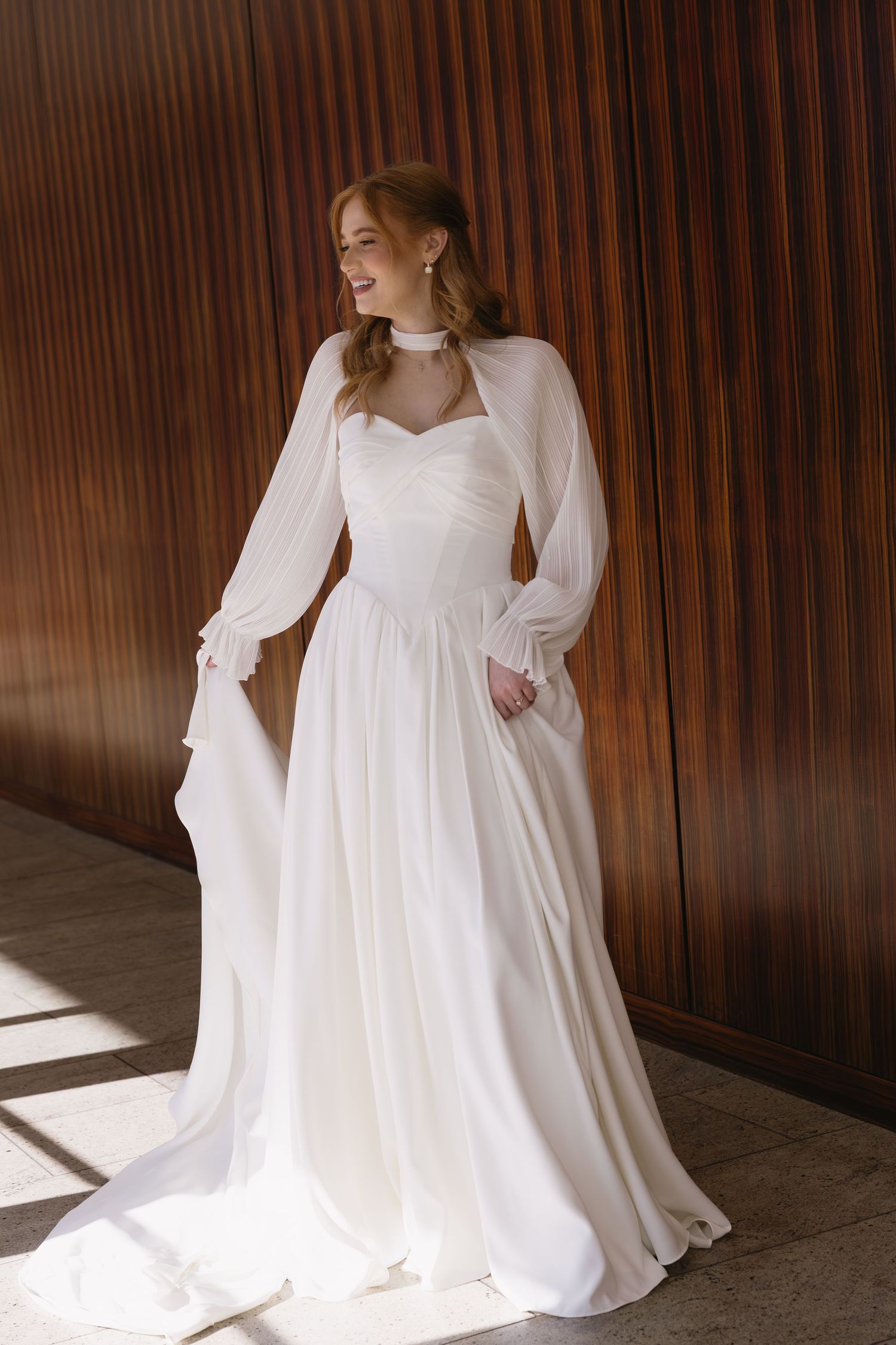 A flowing white wedding gown with dramatic sleeves photographed against wooden paneled walls.