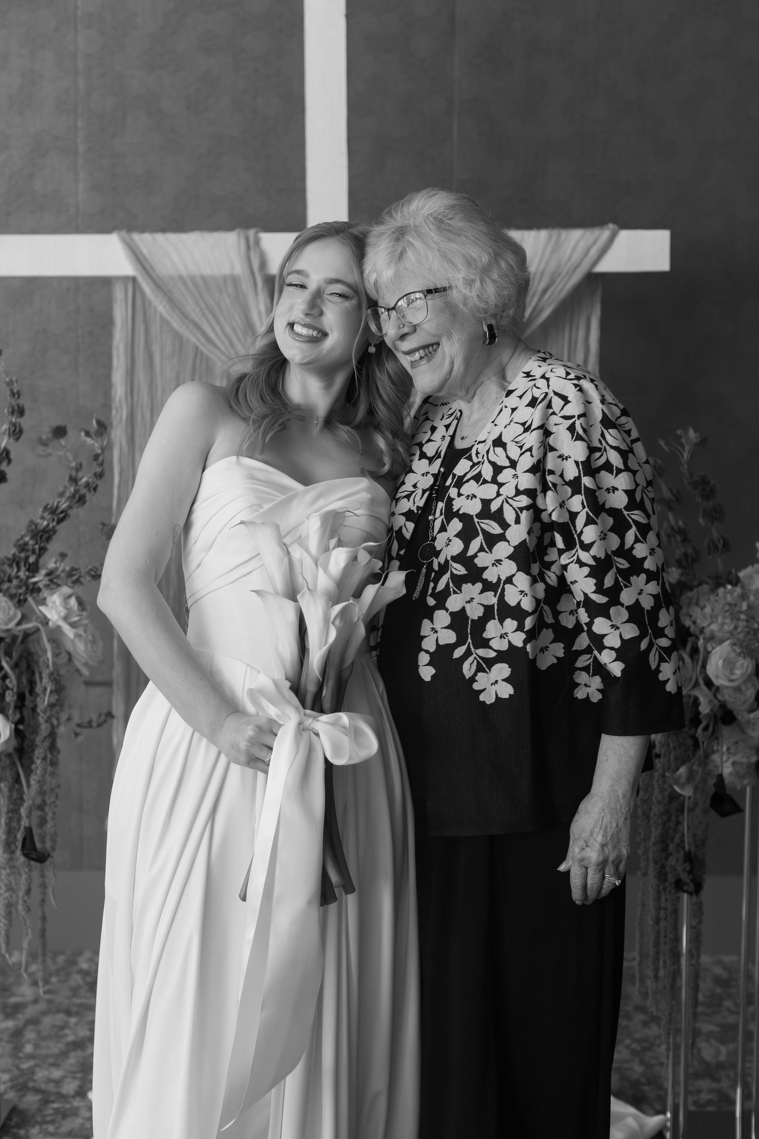 Black and white photo of wedding party with floral arrangements in an elegant setting.