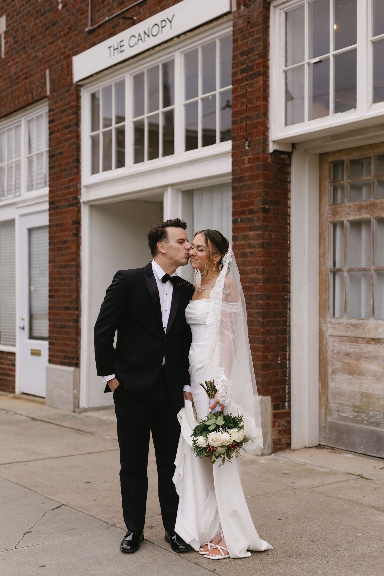 Wedding couple sharing a tender moment outside a brick building with white trim.