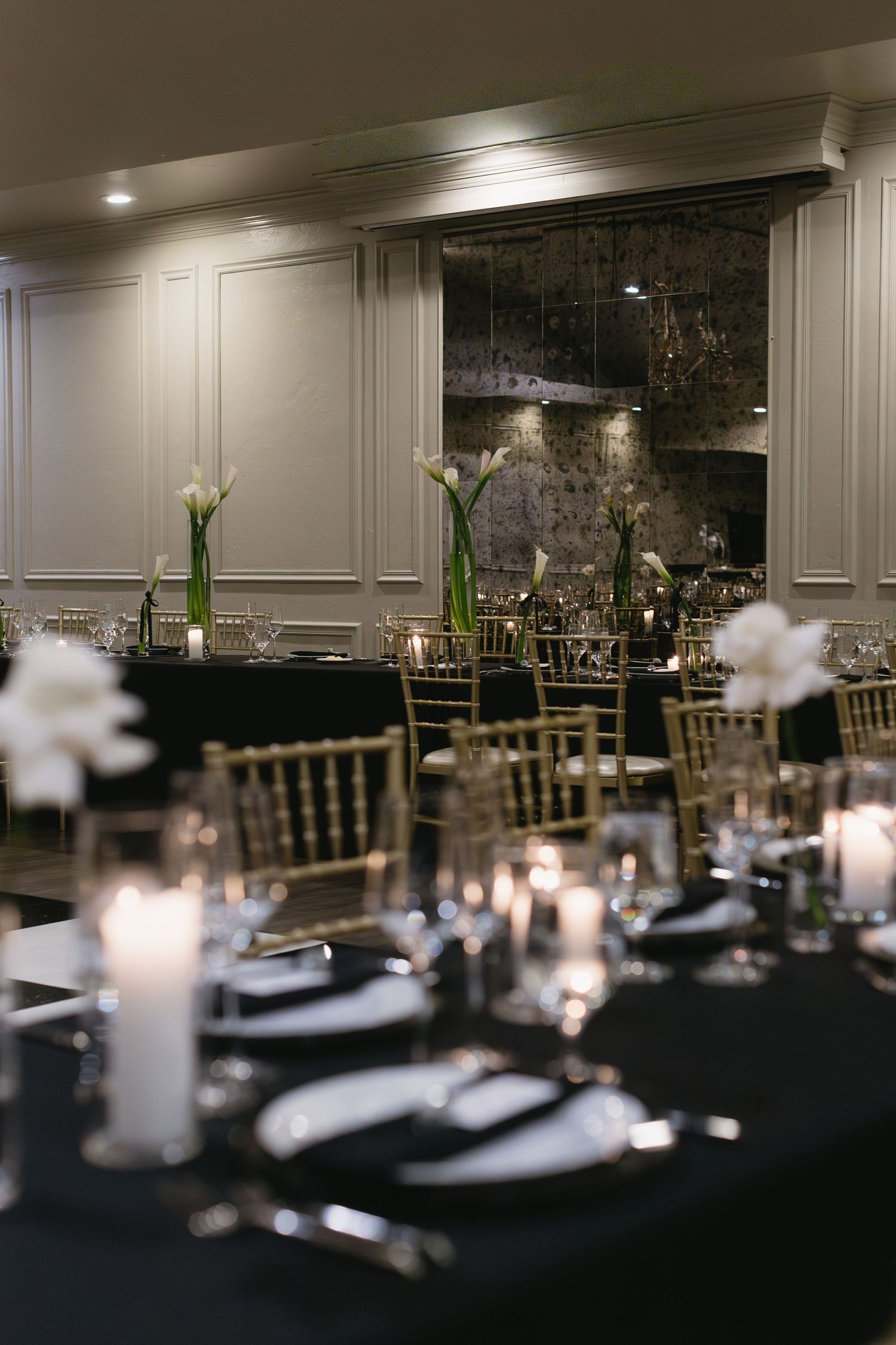 Formal dining table with black linens, gold chairs, and tall white floral centerpieces in an elegant room.
