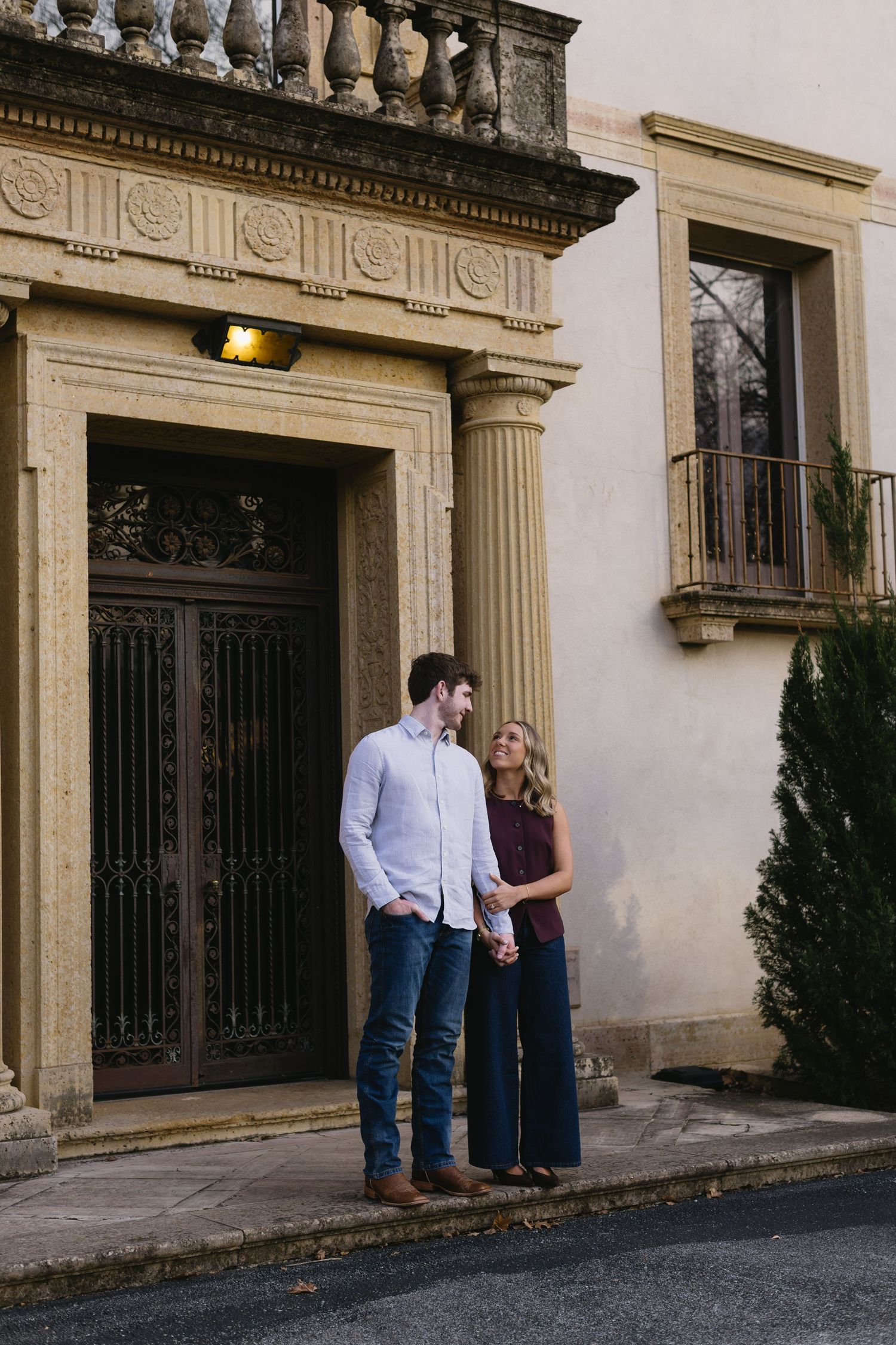 A couple stands together in front of an ornate doorway with classical architectural details.