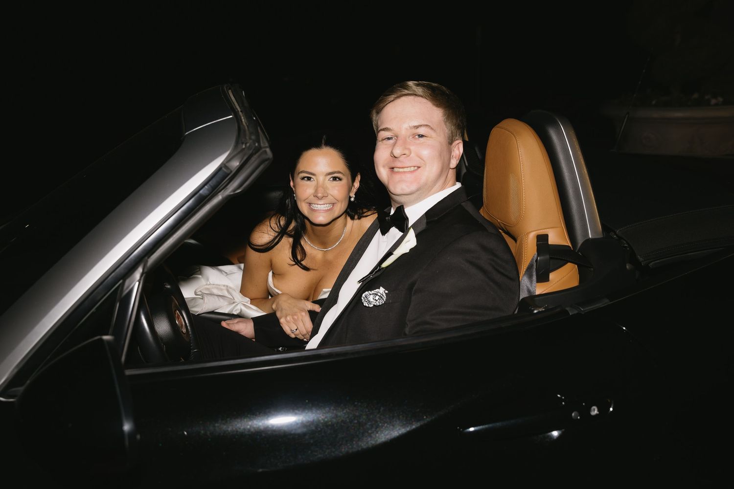Couple departing wedding reception in dark car at night.