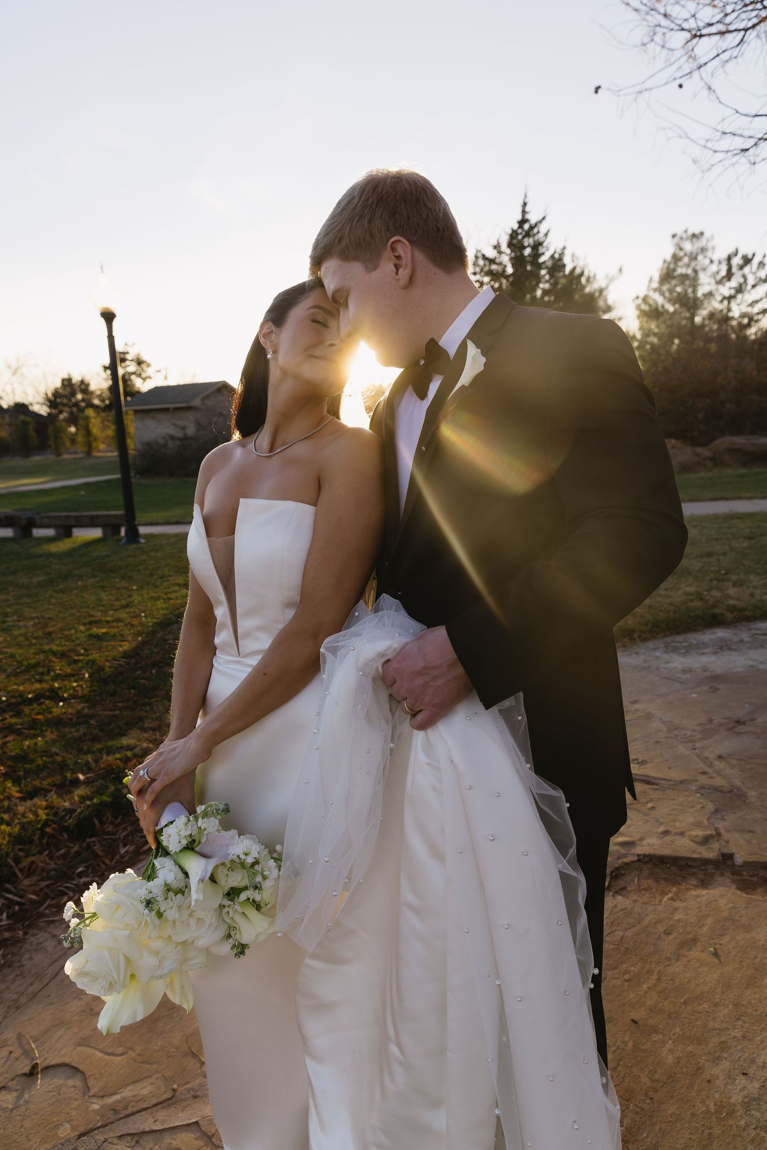 Romantic sunset wedding portrait with white bouquet and flowing dress.
