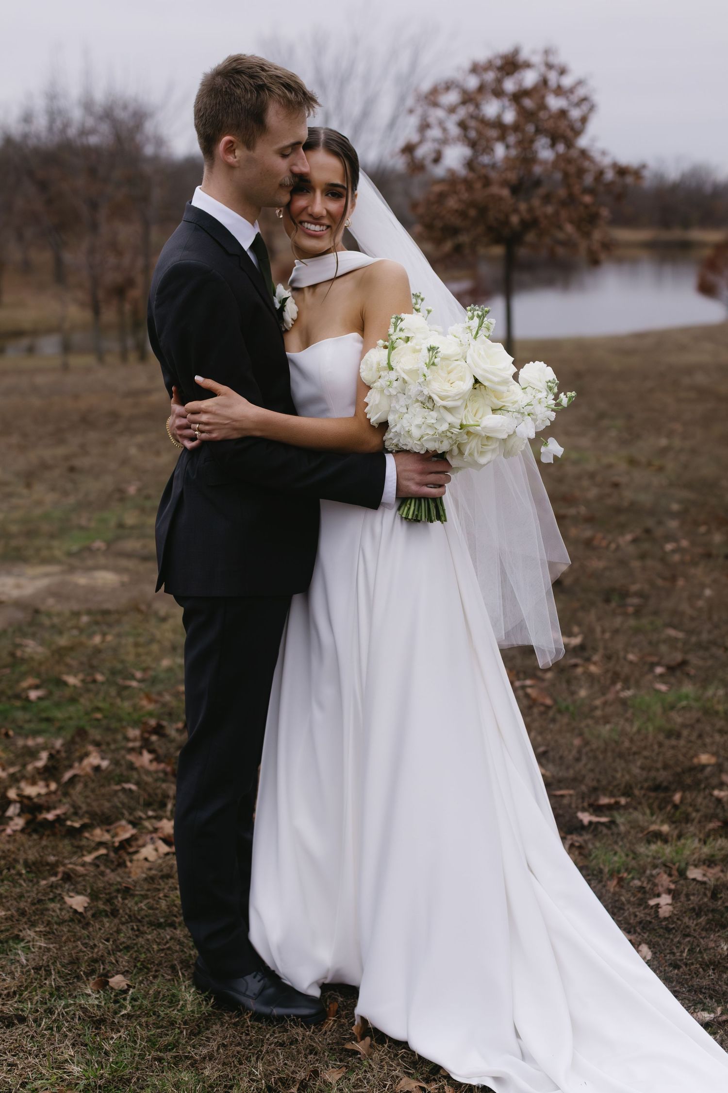 Romantic outdoor wedding portrait with bride in white gown holding bouquet among autumn leaves.