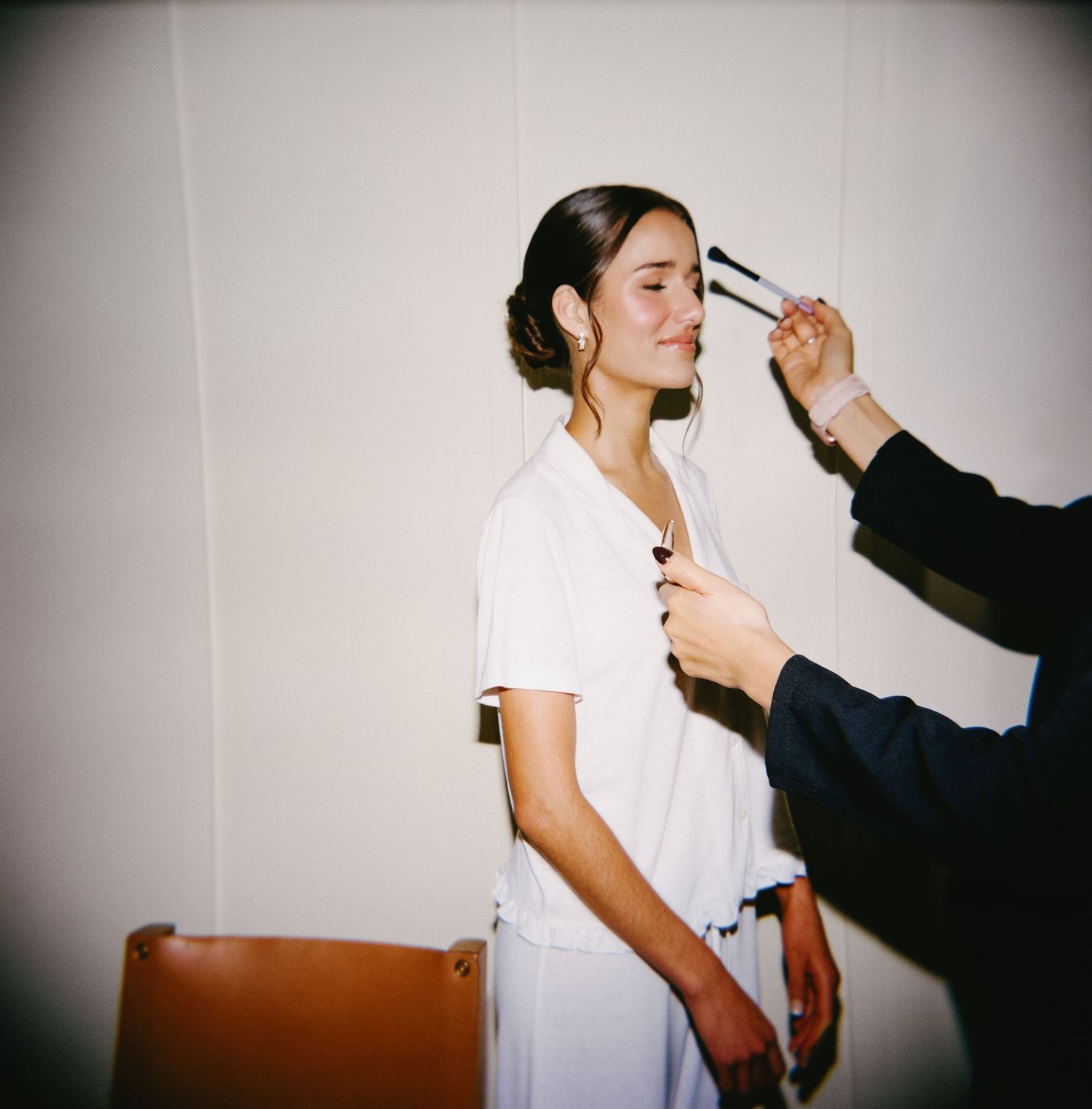 Behind-the-scenes wedding preparation showing makeup application in a bright room.