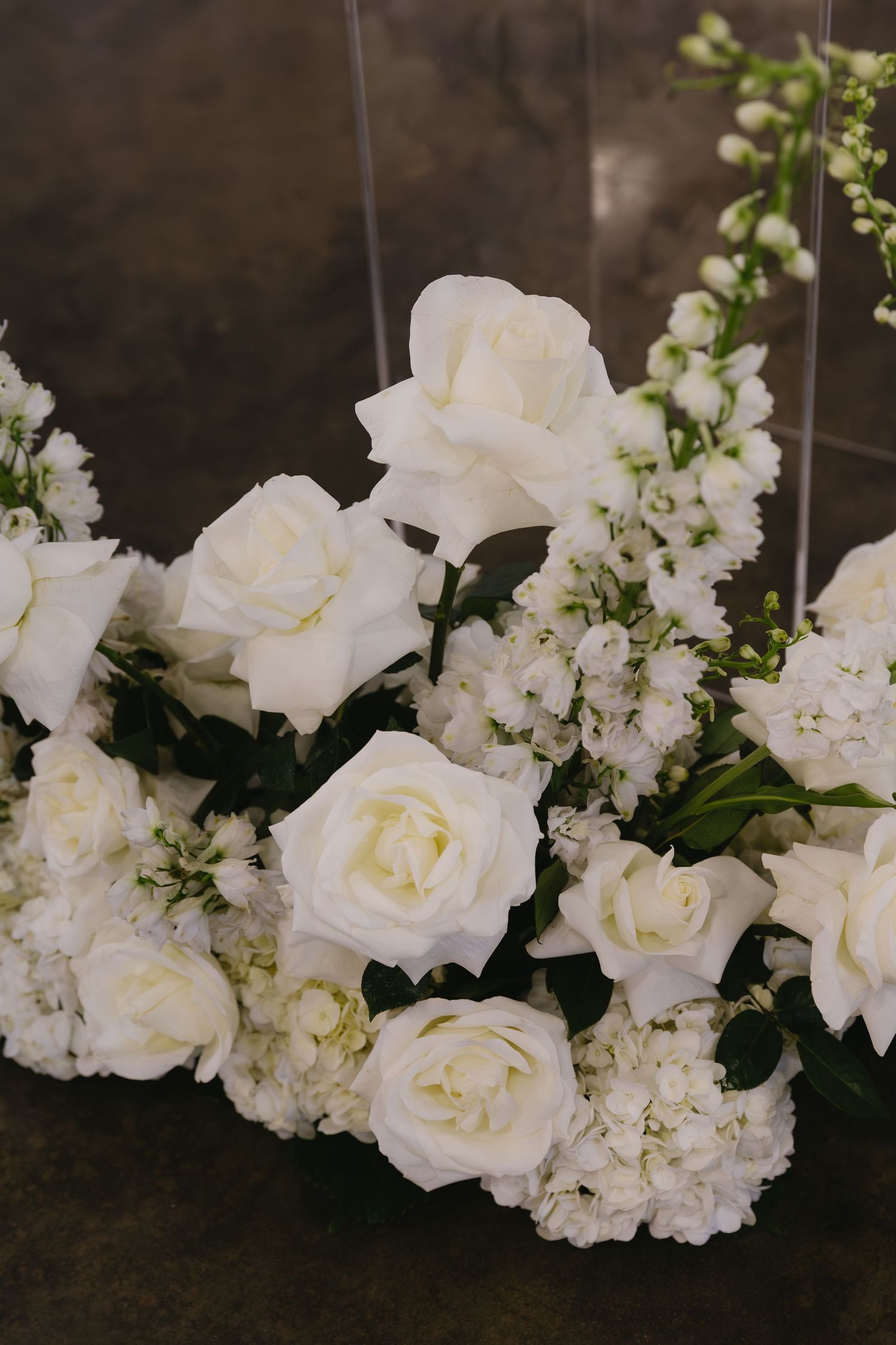 Delicate white roses and flowers arranged in an elegant cascading display against a dark background.