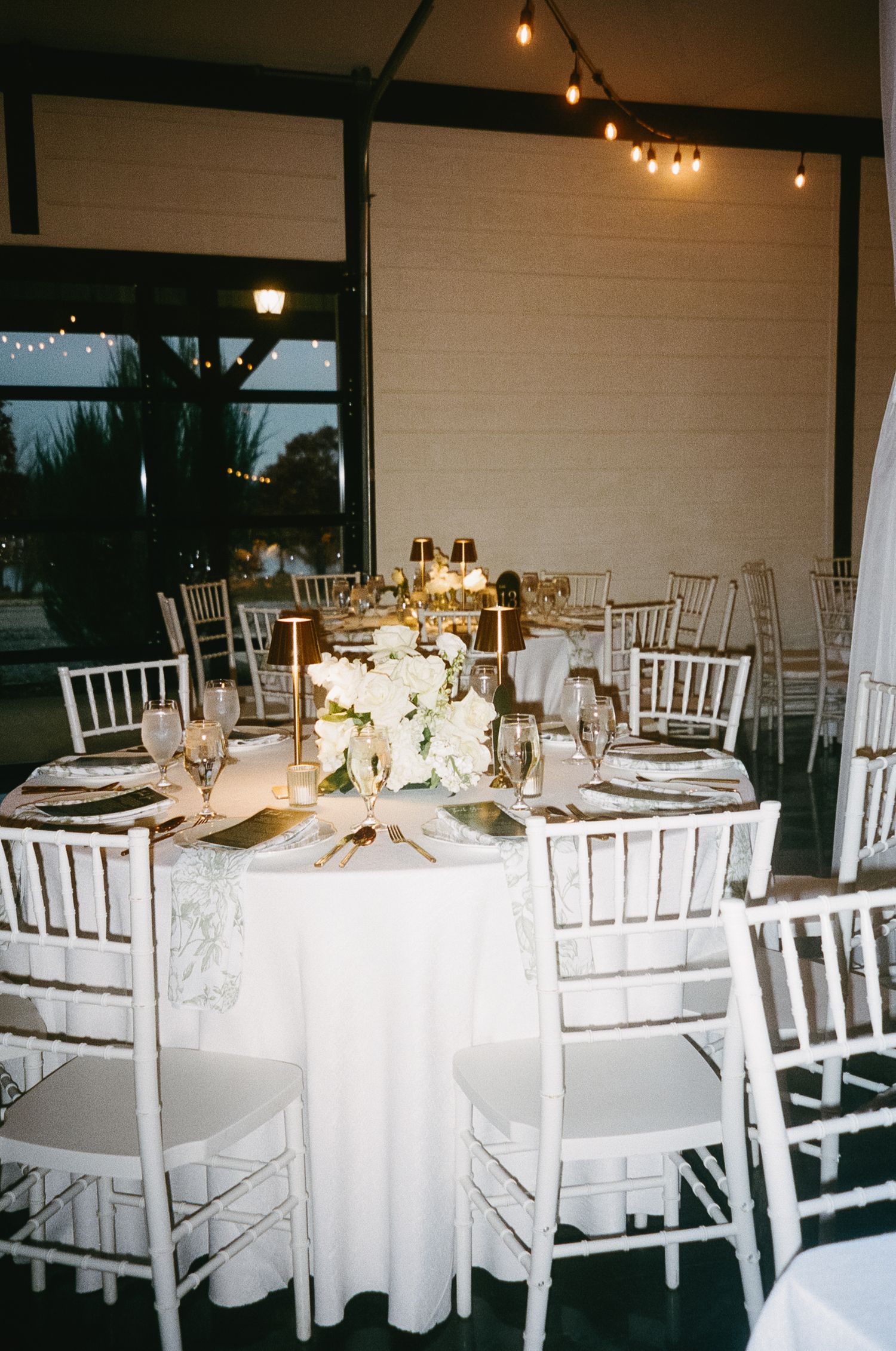 Elegant wedding reception setup with white chiavari chairs and round tables with white linens.