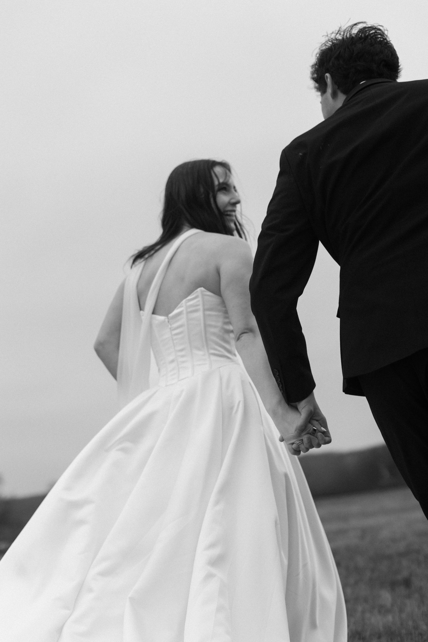 Back view of bride in structured white wedding gown walking across misty field.
